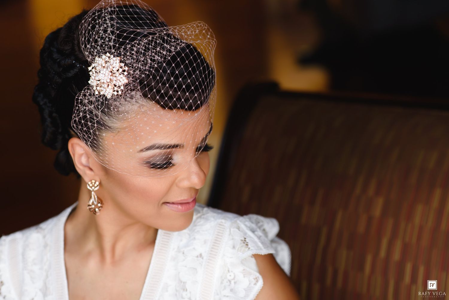 Bride wearing birdcage veil with floral brooch, elegant drop earrings, and white lace dress on her wedding day.