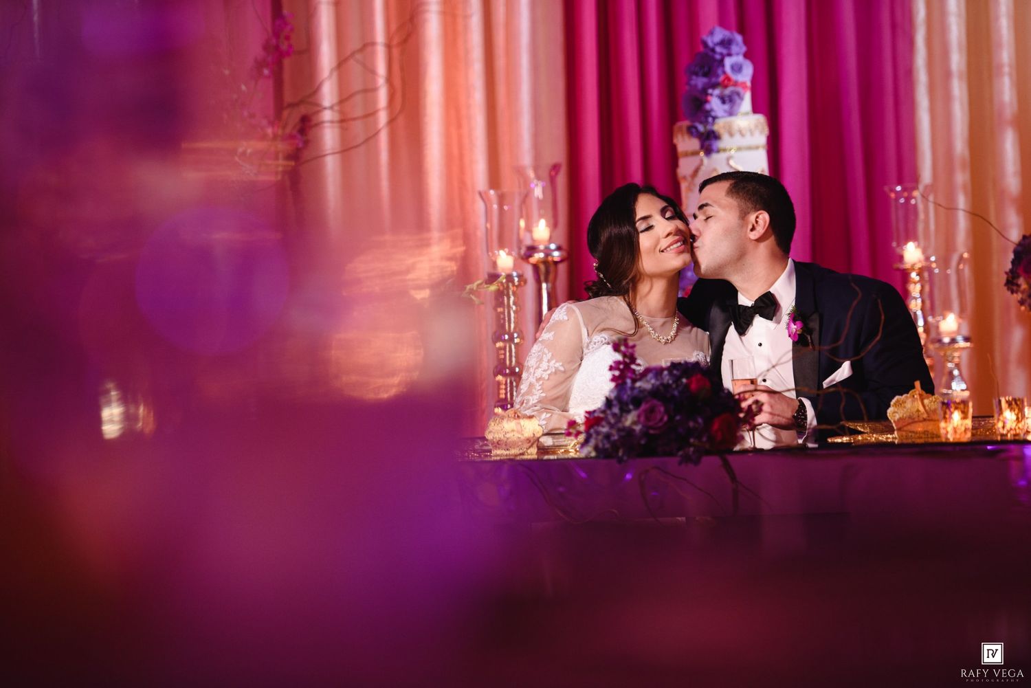 Bride and groom share a romantic moment at their wedding reception, surrounded by candlelight and purple floral decor.