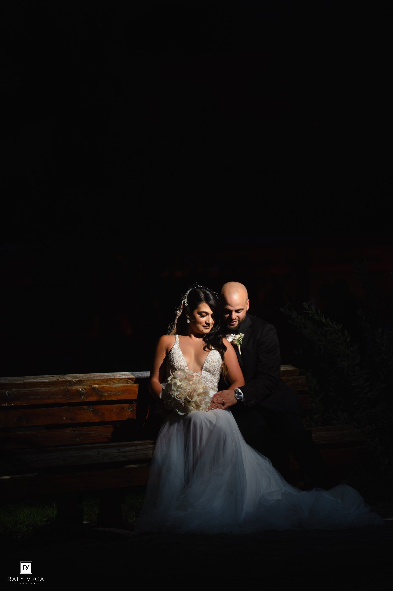 Bride and groom share a romantic embrace in dramatic dark lighting at their wedding night portrait session.