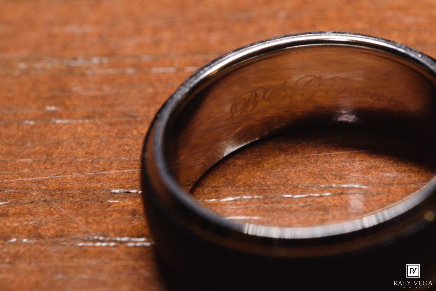 Close-up of a dark wooden wedding band with engraving on a wooden surface.