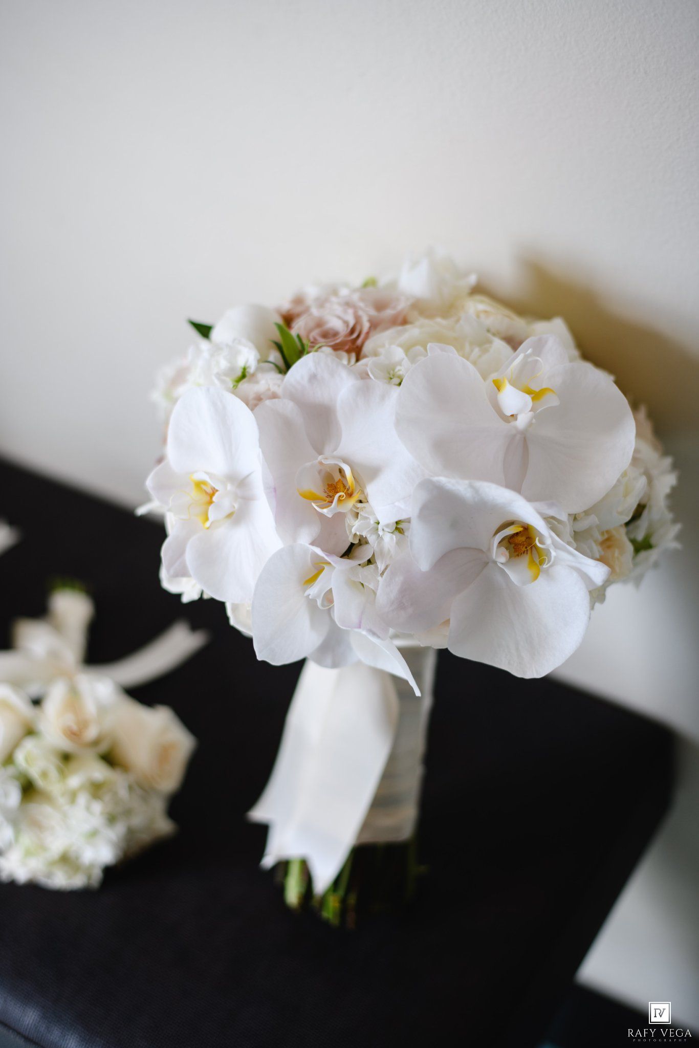 Elegant bridal bouquet of white phalaenopsis orchids wrapped in white ribbon on dark surface.