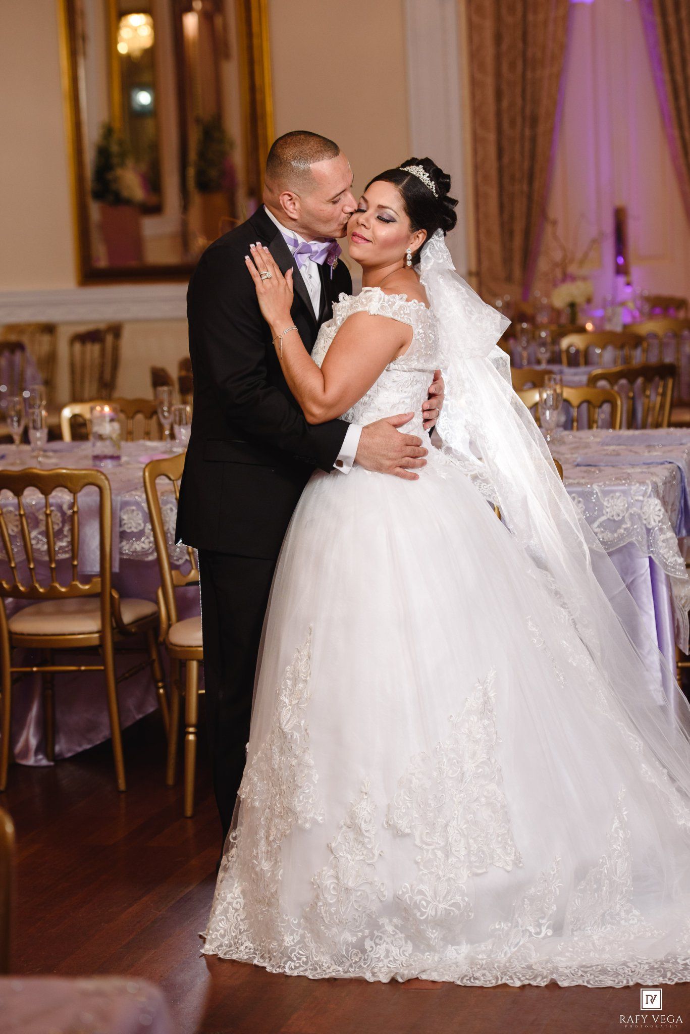 Bride in white ball gown and groom in black tuxedo share a romantic embrace on the dance floor at their wedding reception.
