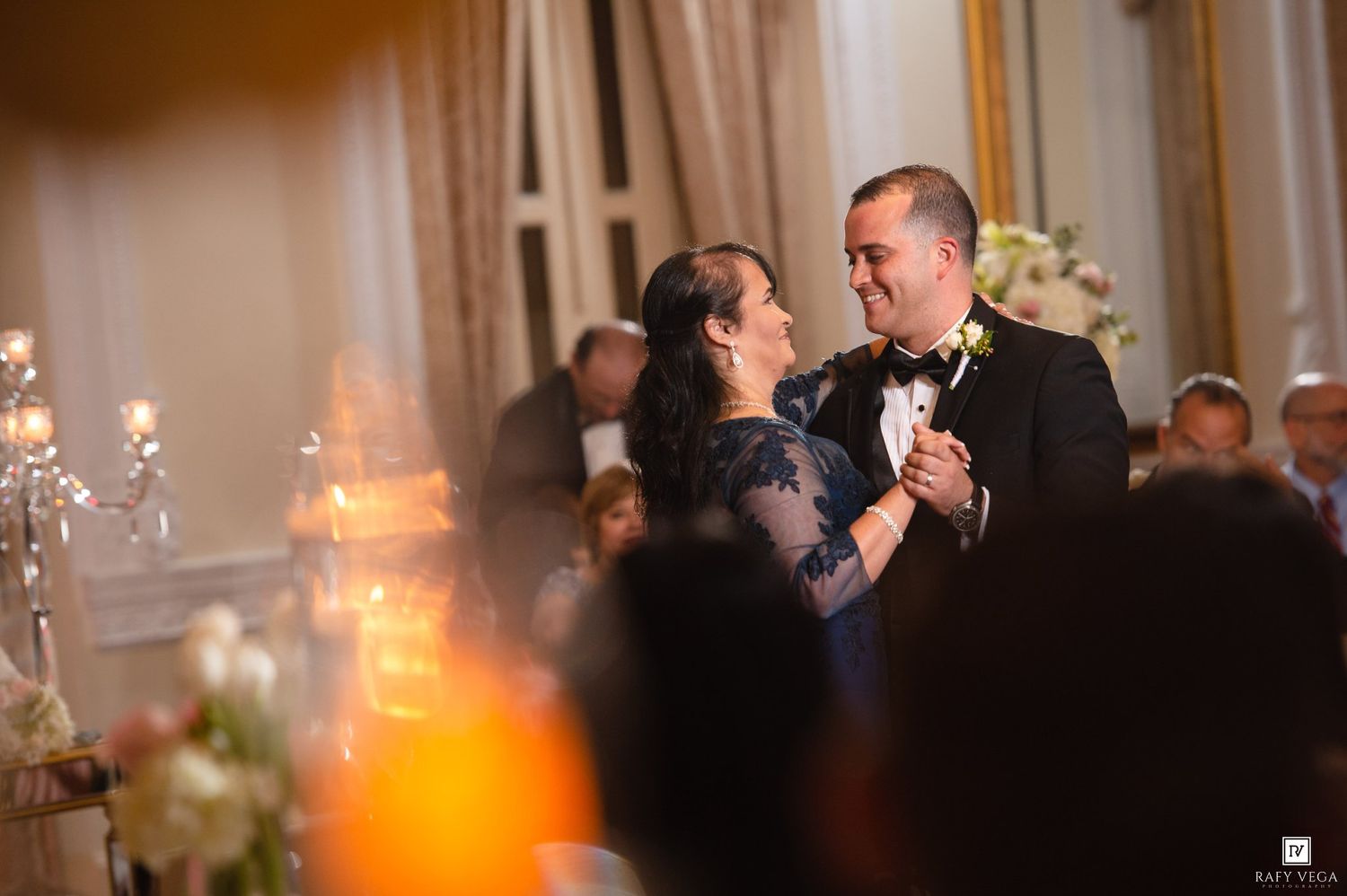 Couple shares romantic first dance at elegant wedding reception with candlelit chandeliers and floral arrangements.
