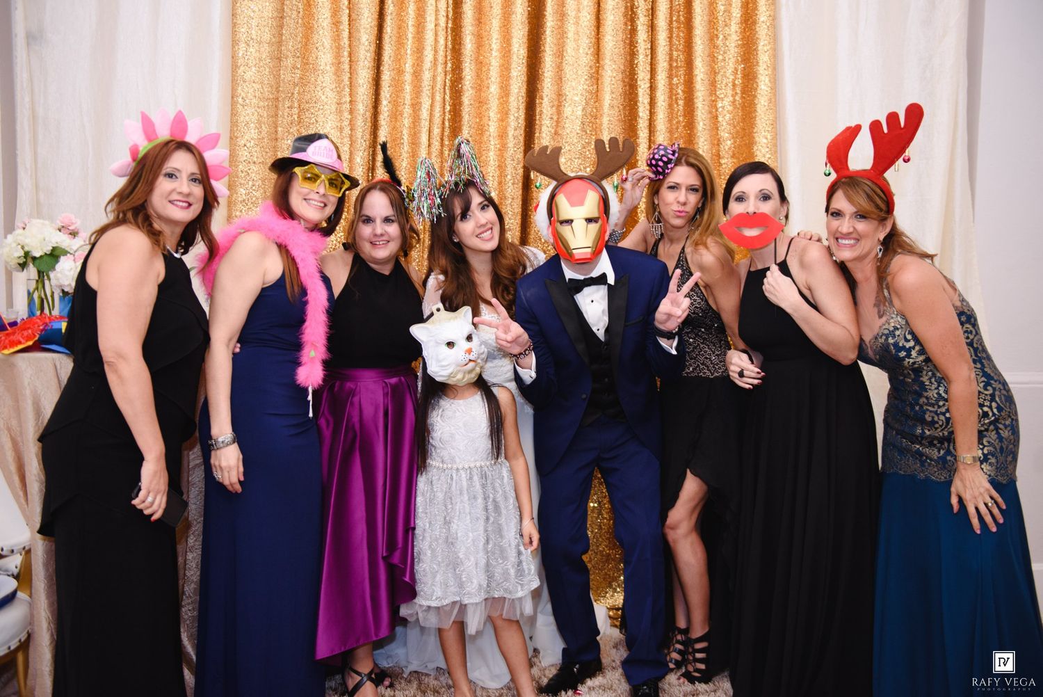 Group of elegantly dressed people posing with fun masks and props at a formal party event.