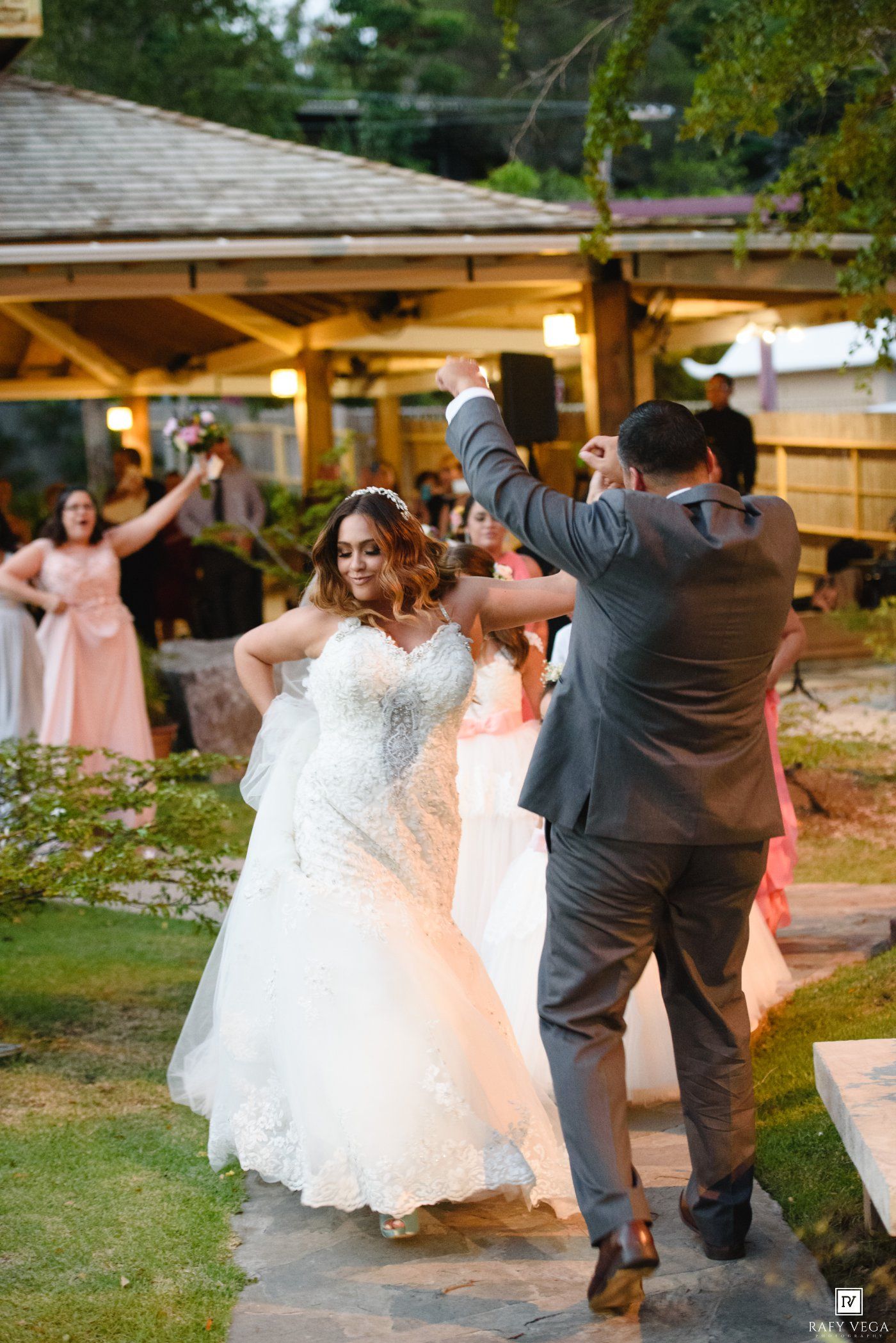 Bride and groom share their first dance outdoors at a wedding reception surrounded by guests in formal attire.