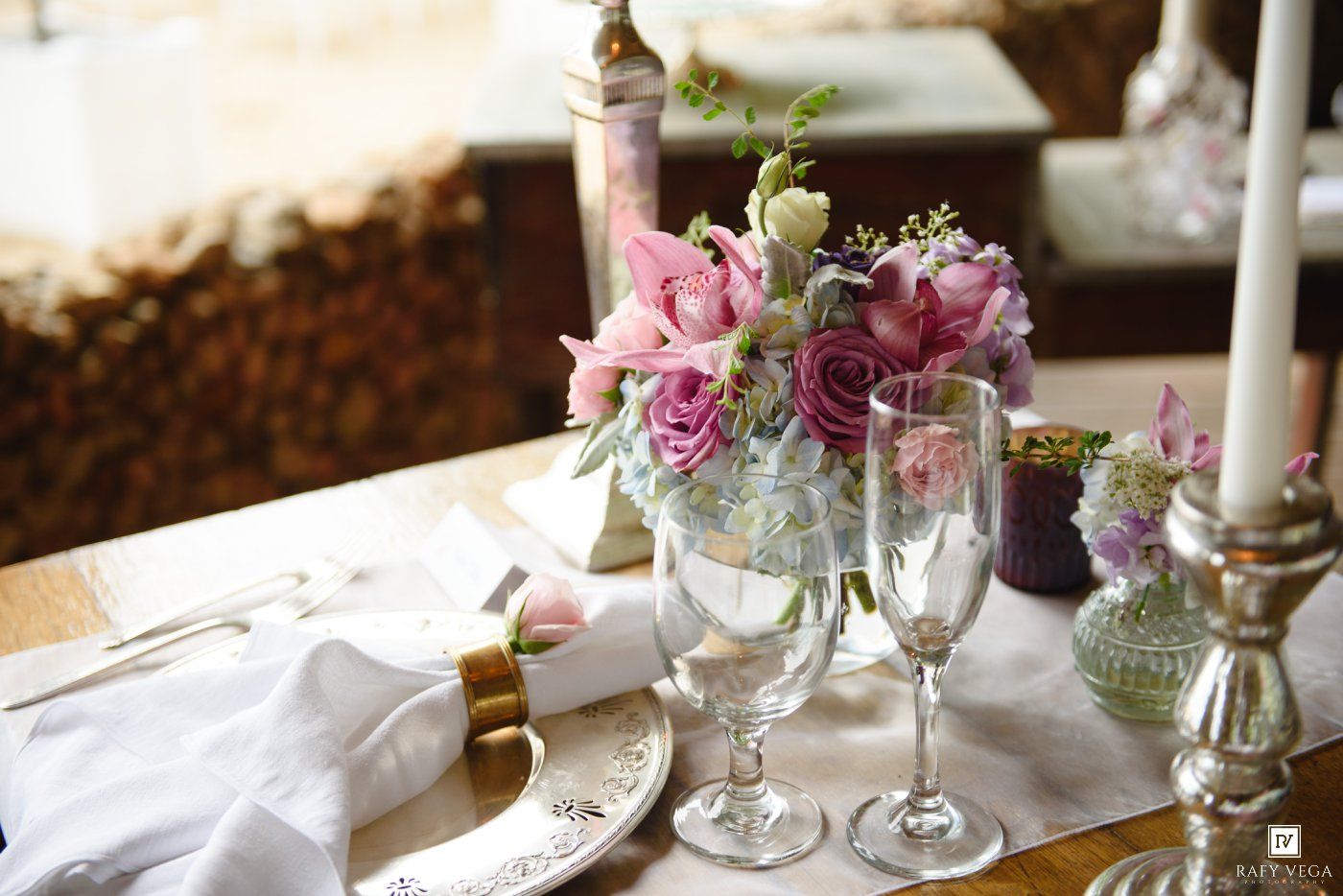 Elegant wedding table setting with pink floral centerpiece, crystal champagne flutes, white napkins, and silver candleholders.