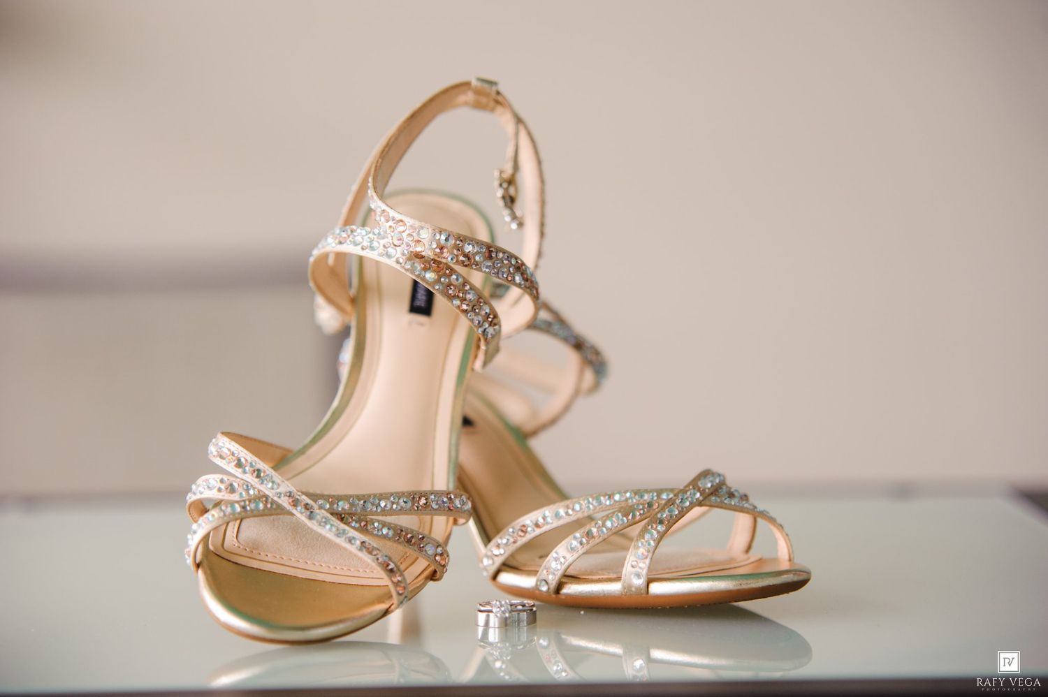 Elegant gold strappy heeled sandals with crystal embellishments displayed on a reflective surface.