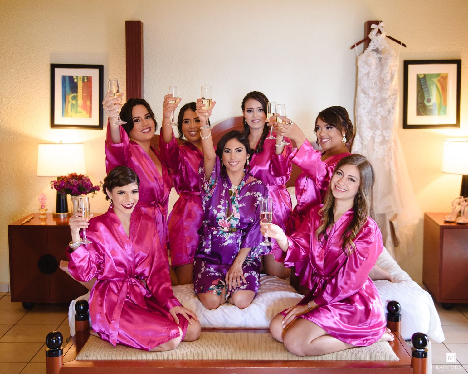 Bride and bridesmaids in pink satin robes celebrating together on a bed before the wedding ceremony.