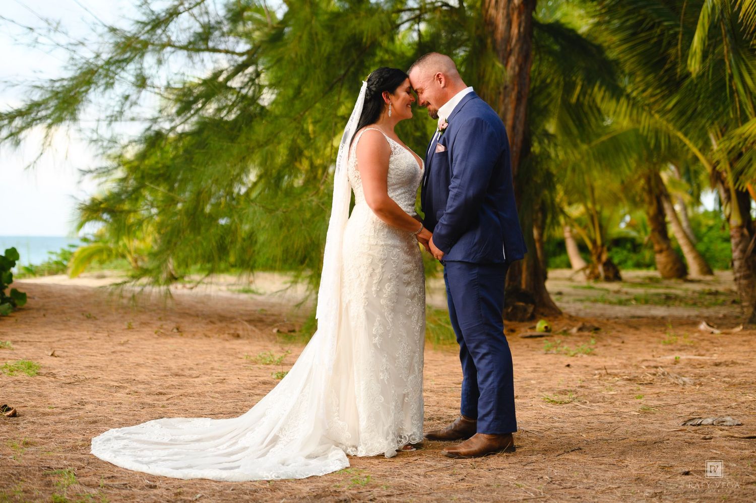 Bride and groom share a romantic moment under tropical palm trees on a sandy beach in a destination wedding.