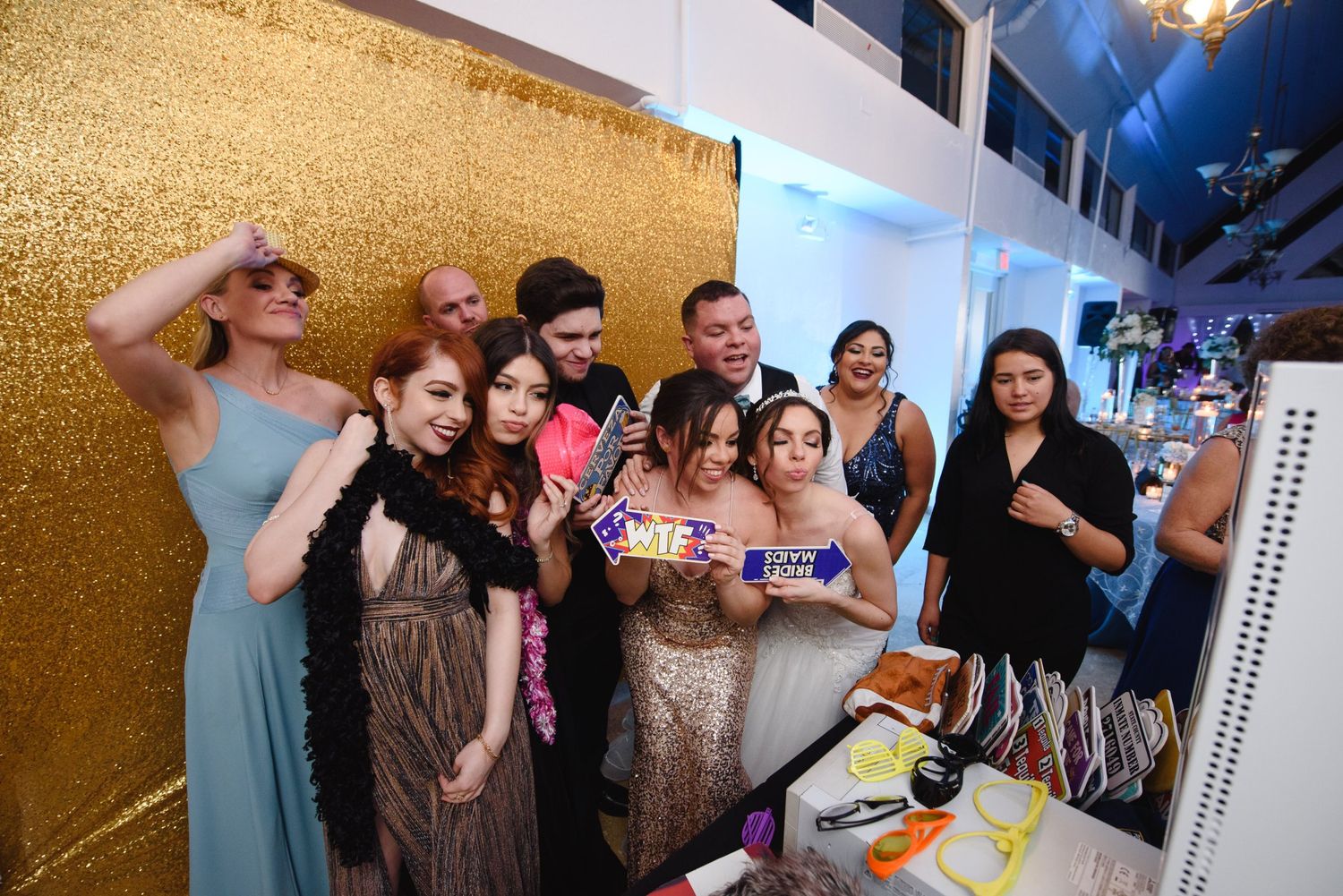 Group of friends posing together at a glamorous party with gold sequin backdrop, holding props and smiling.