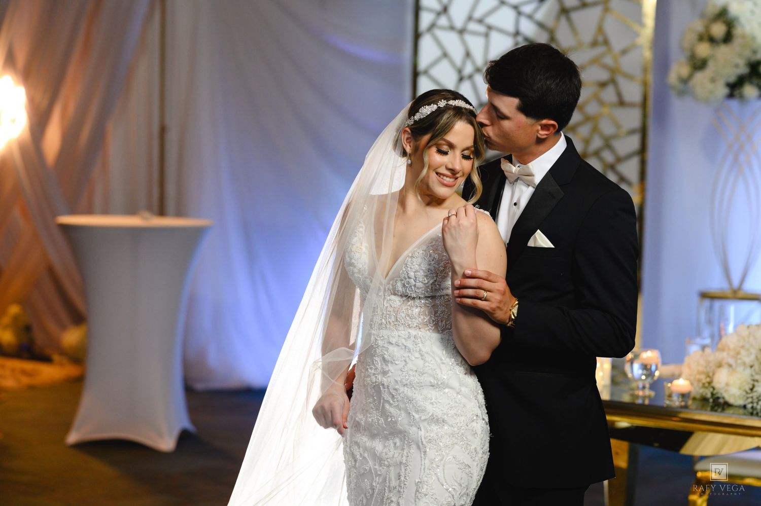 Bride in beaded gown and veil shares first dance with groom in black tuxedo at elegant wedding reception.
