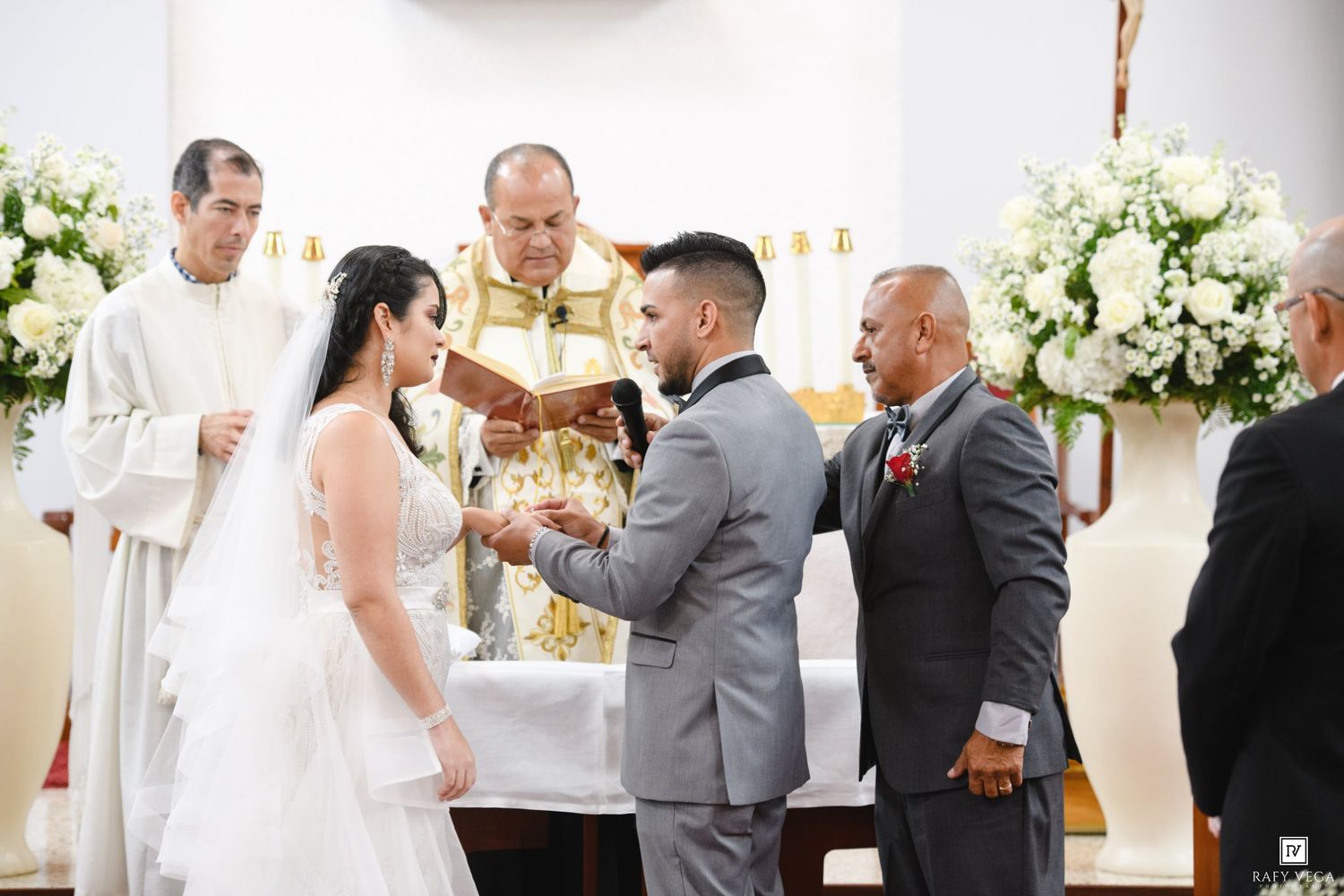 Bride and groom exchange rings at church altar during wedding ceremony with officiant and best man present.