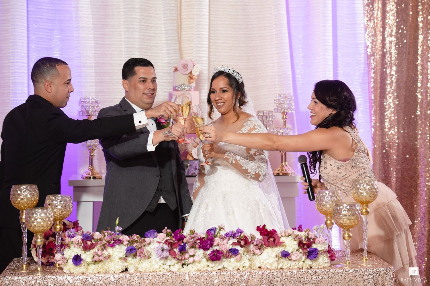 Wedding party raises champagne glasses in a toast at a glamorous reception with floral decor.