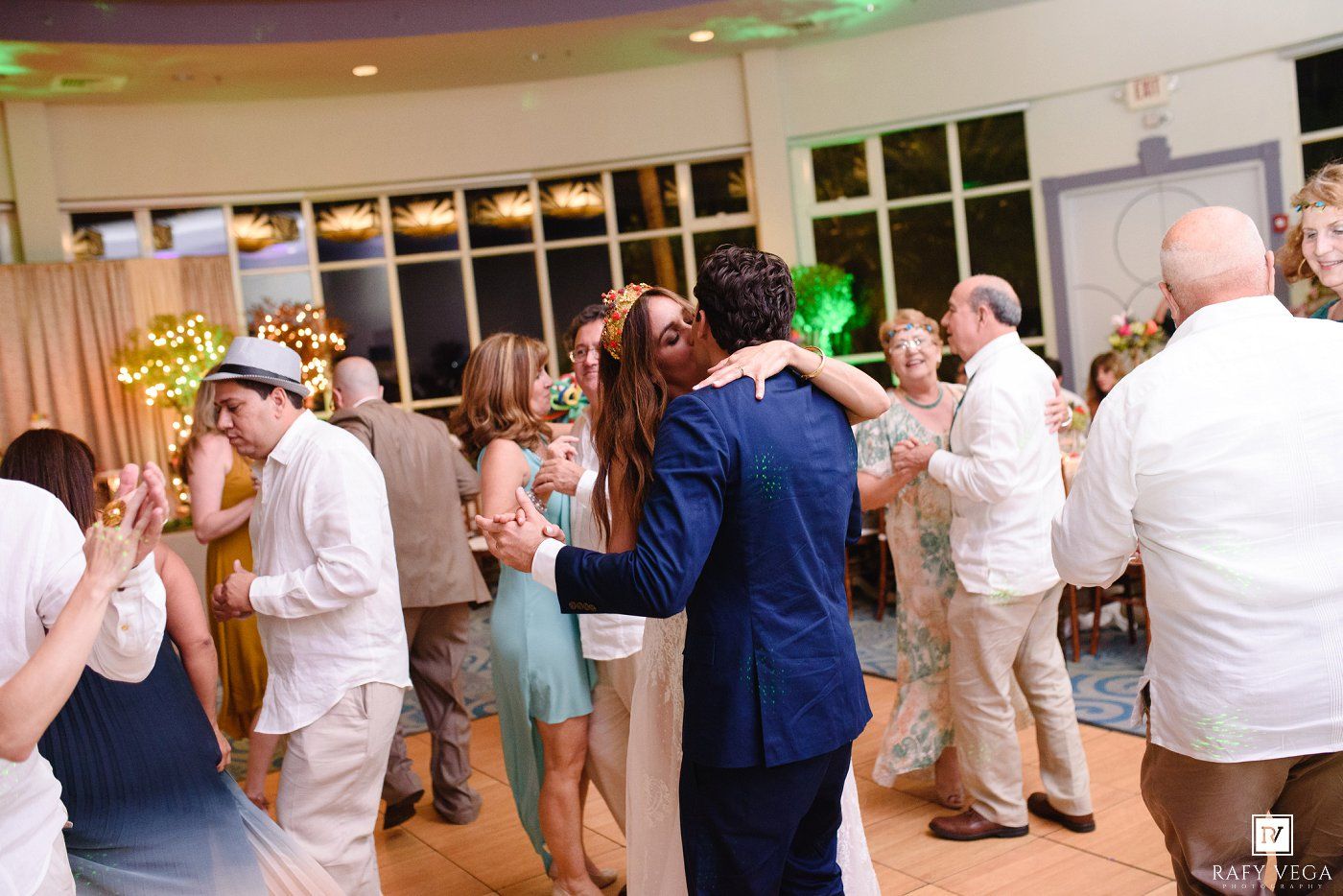 Guests dancing joyfully at an elegant wedding reception with green ambient lighting and festive decor.