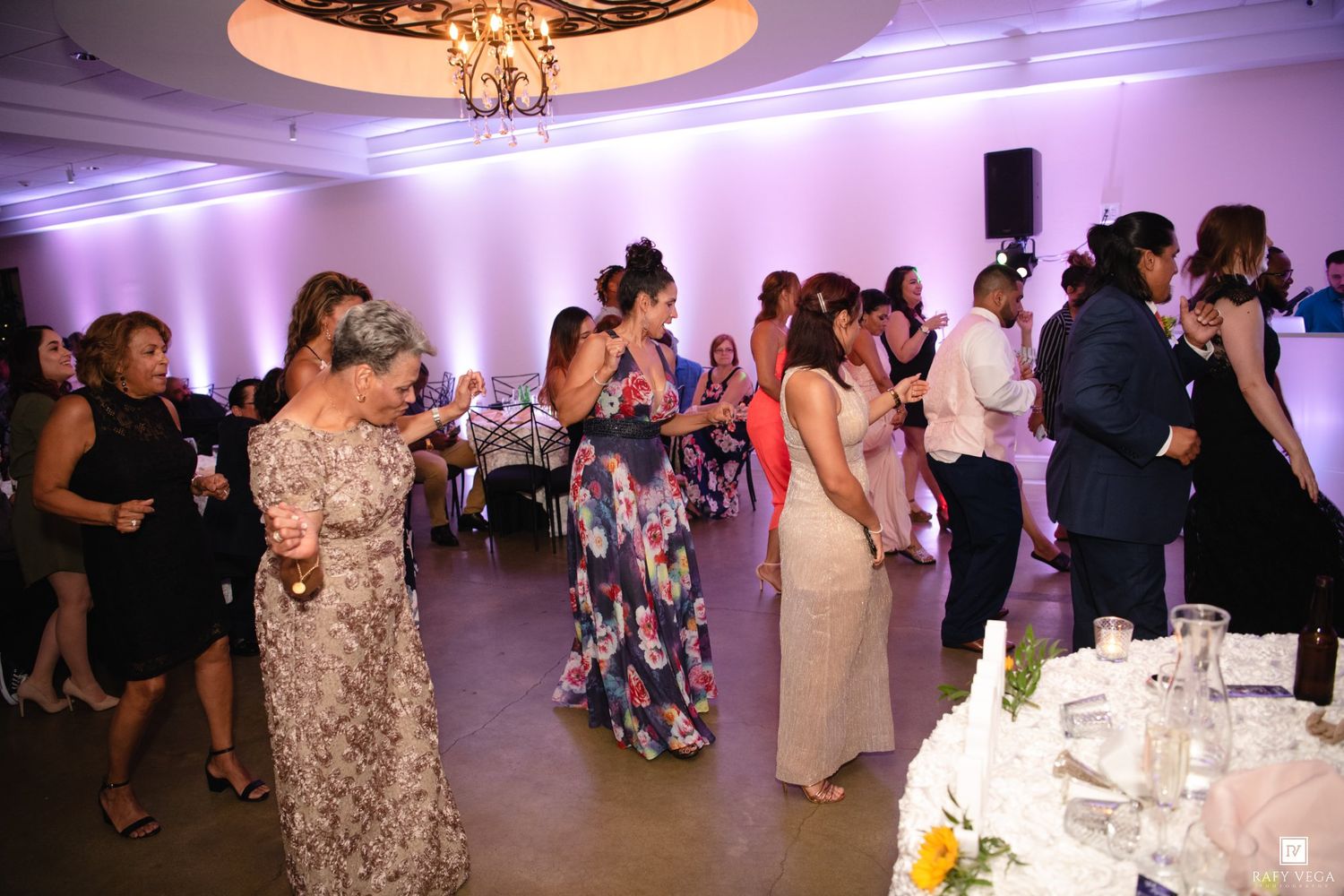 Guests mingling and dancing in an elegant ballroom with purple uplighting at a wedding reception.
