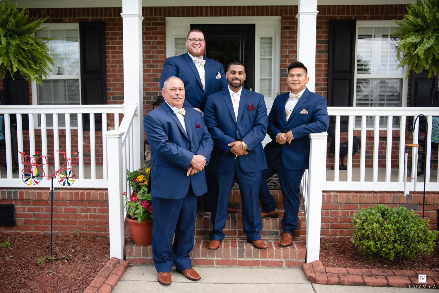 Four men in navy blue suits pose on brick home steps for a formal wedding groomsmen photo.