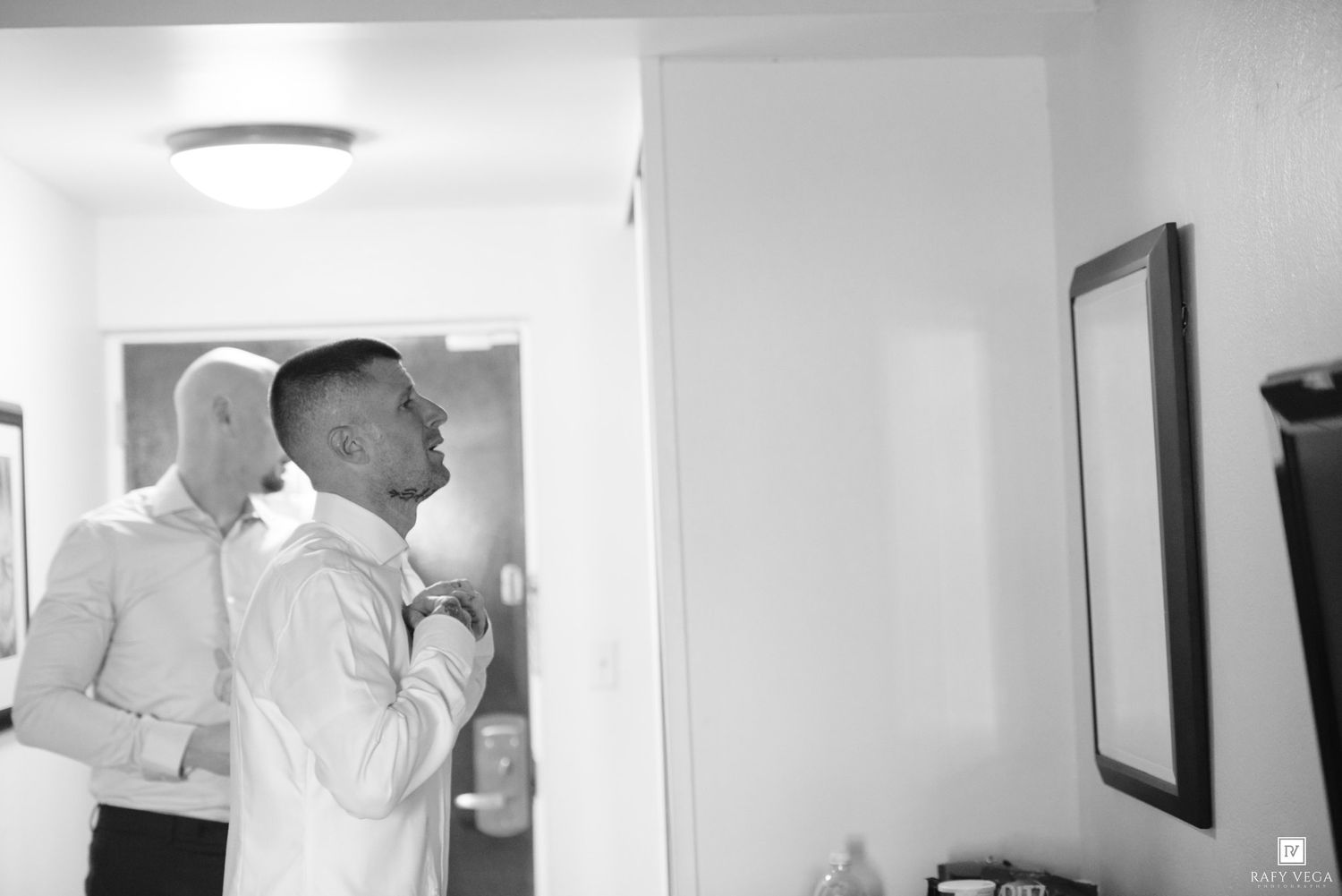 Two men in white dress shirts preparing for a formal event in a black and white candid photograph.