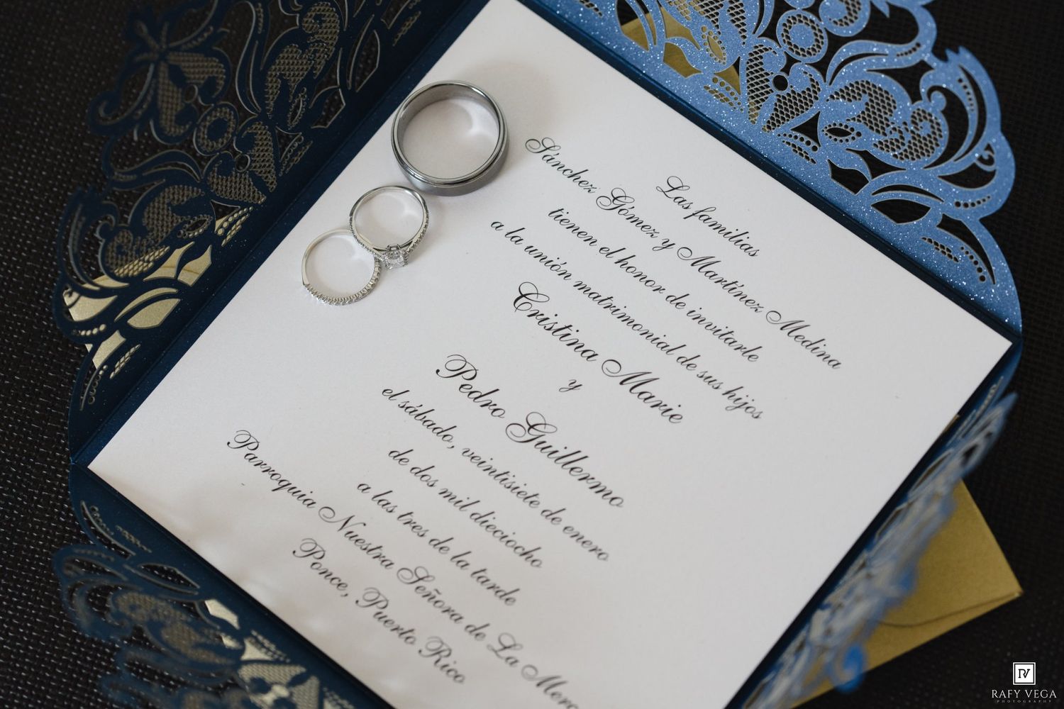 Elegant blue laser-cut wedding invitation with two silver rings resting on white card with formal script text.