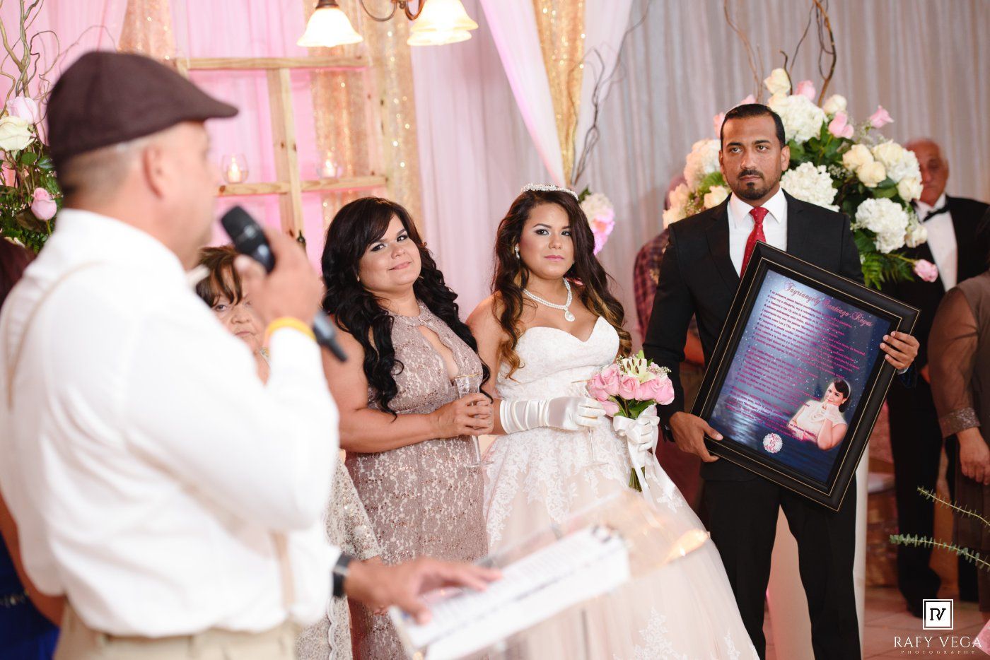 Bride and groom stand at wedding altar as officiant speaks into microphone holding framed photo at elegant ceremony.