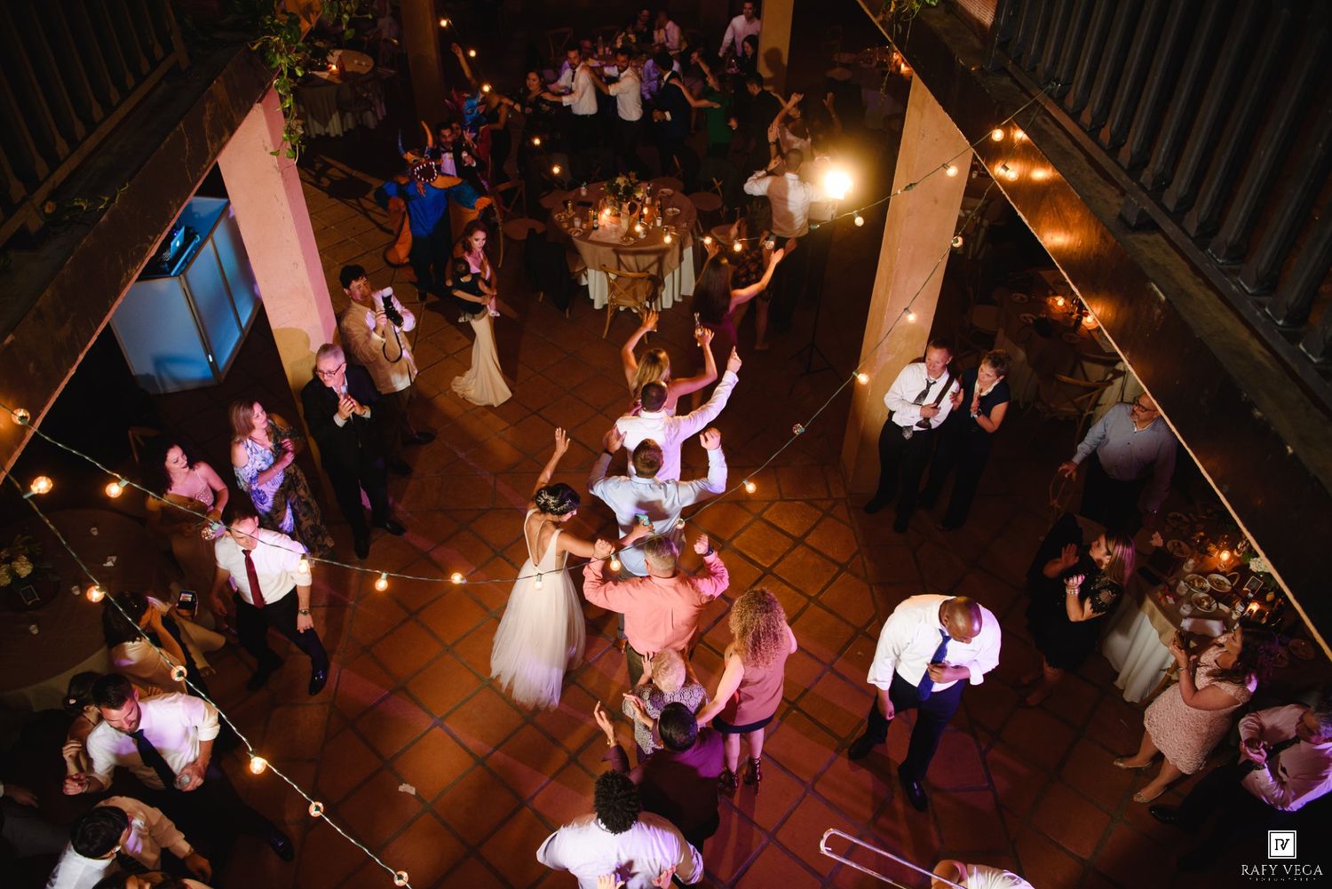 Aerial view of wedding reception guests dancing on a warmly lit dance floor with string lights overhead.