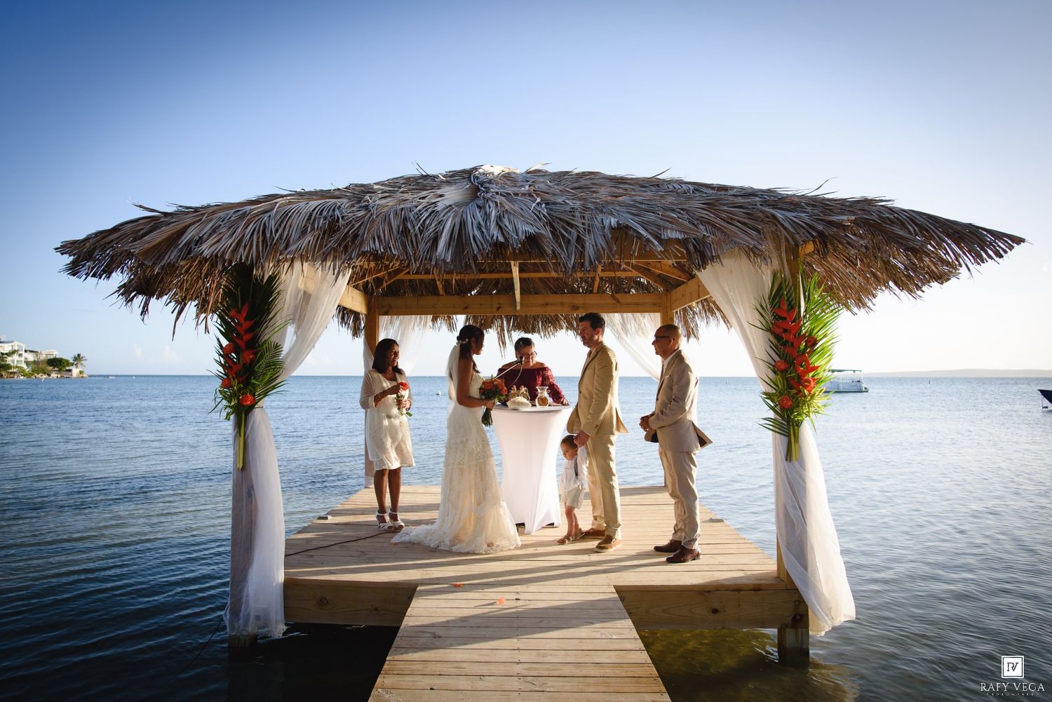 Tropical overwater gazebo wedding ceremony on a wooden dock with ocean views and thatched roof decor.
