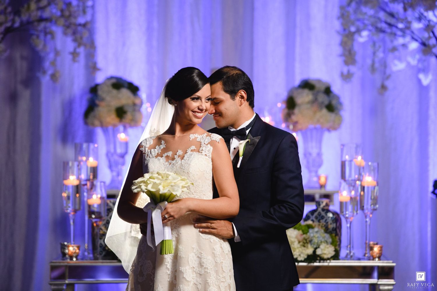 Bride and groom share a romantic moment at elegant wedding altar with candlelight and floral arrangements.