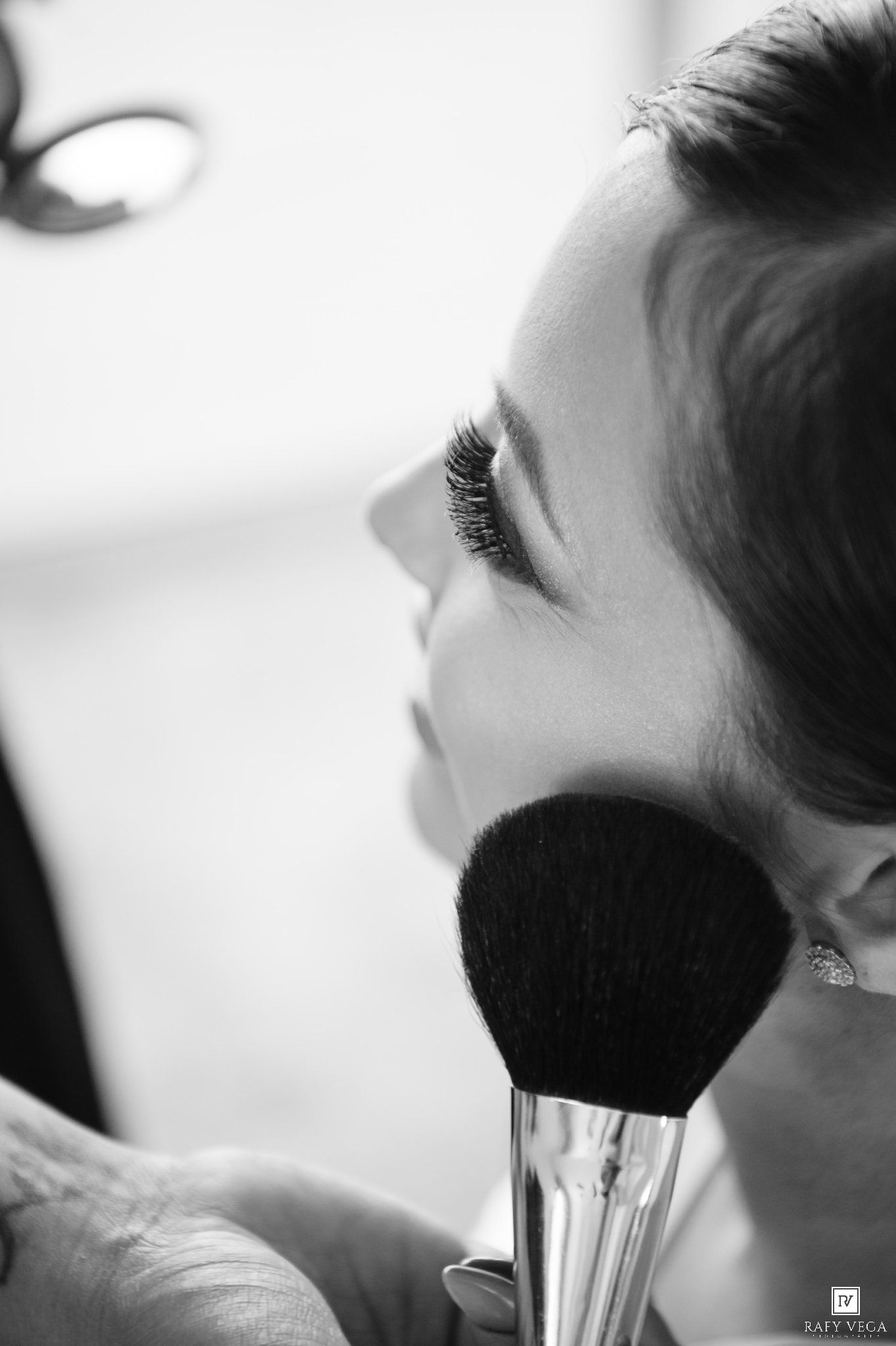 Black and white photo of a woman having makeup applied with a large powder brush during a beauty session.