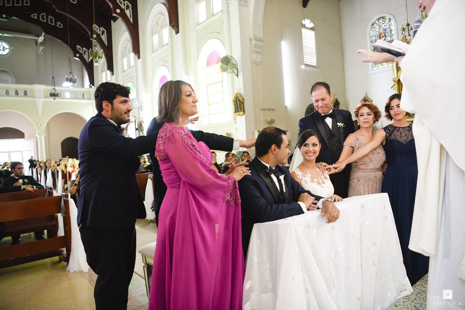 Wedding ceremony in a church with bride and groom at altar surrounded by family and officiant.