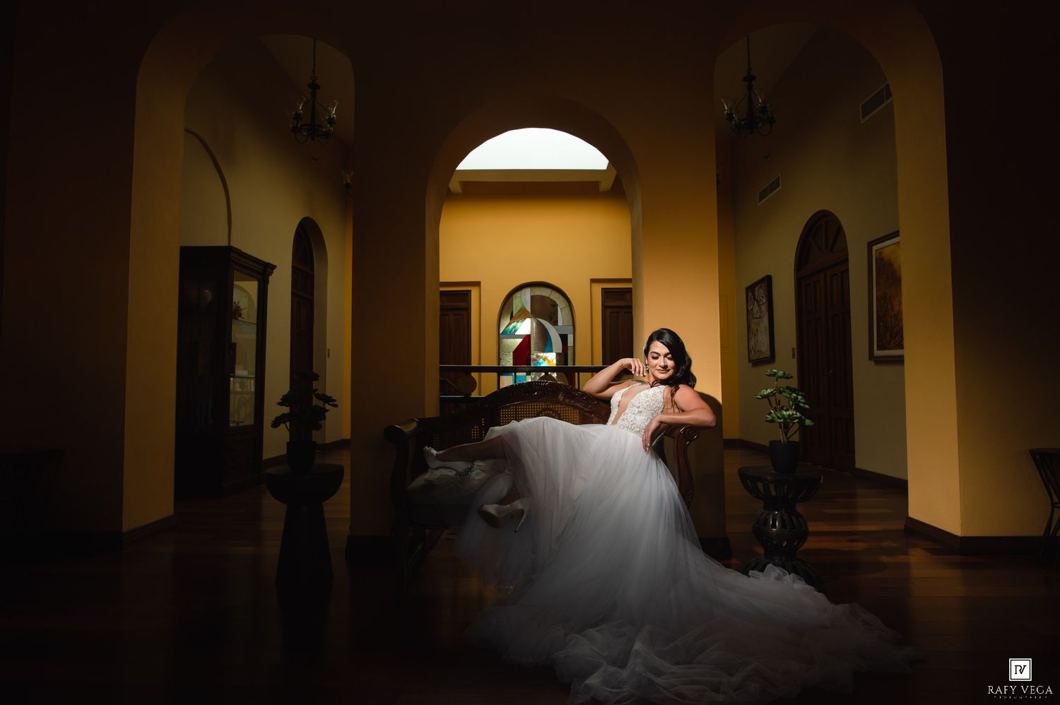 Bride in a white ballgown wedding dress poses elegantly in a grand villa hallway with warm golden lighting.