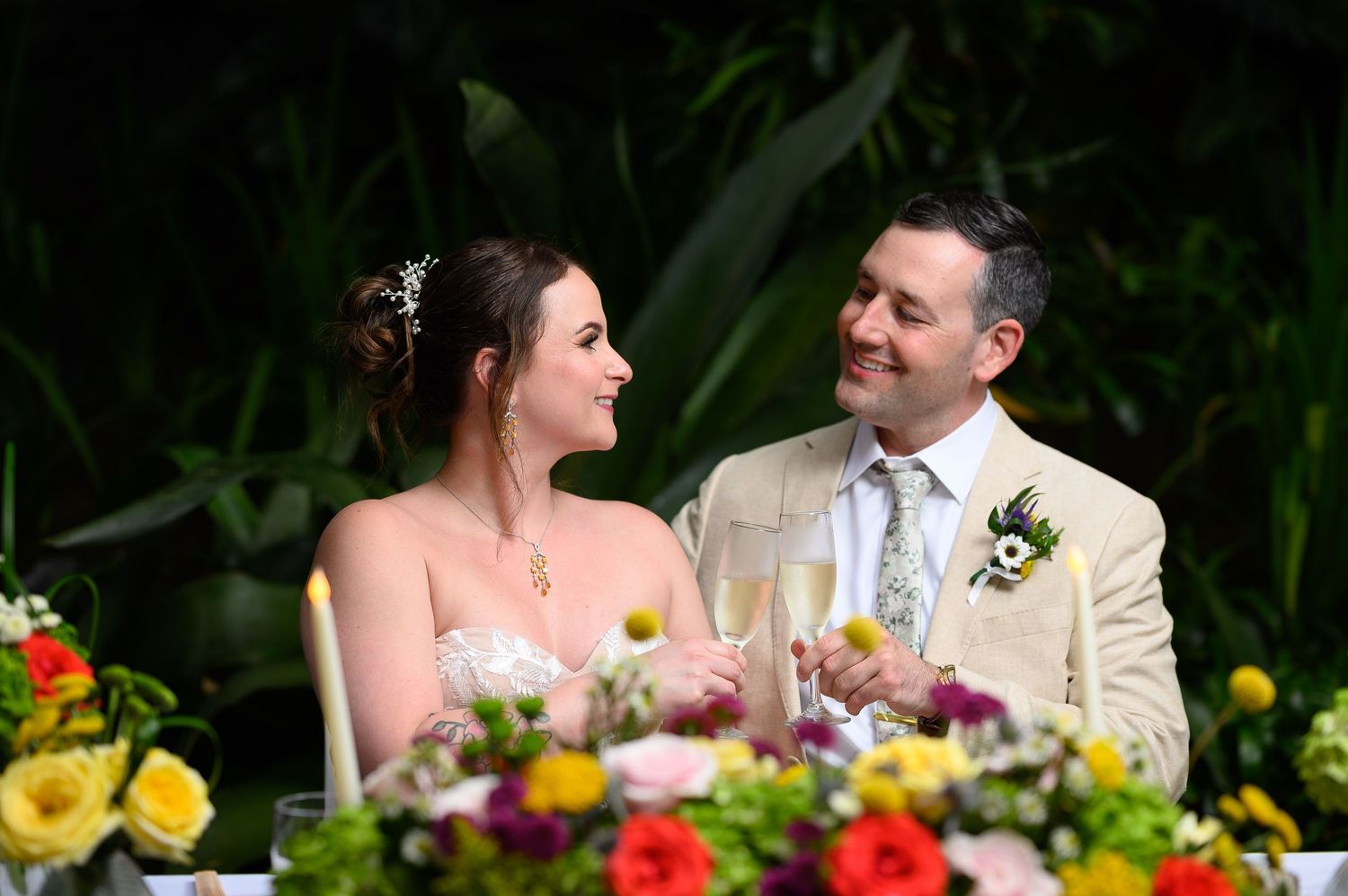 Bride and groom toasting with champagne at floral sweetheart table during outdoor wedding reception.