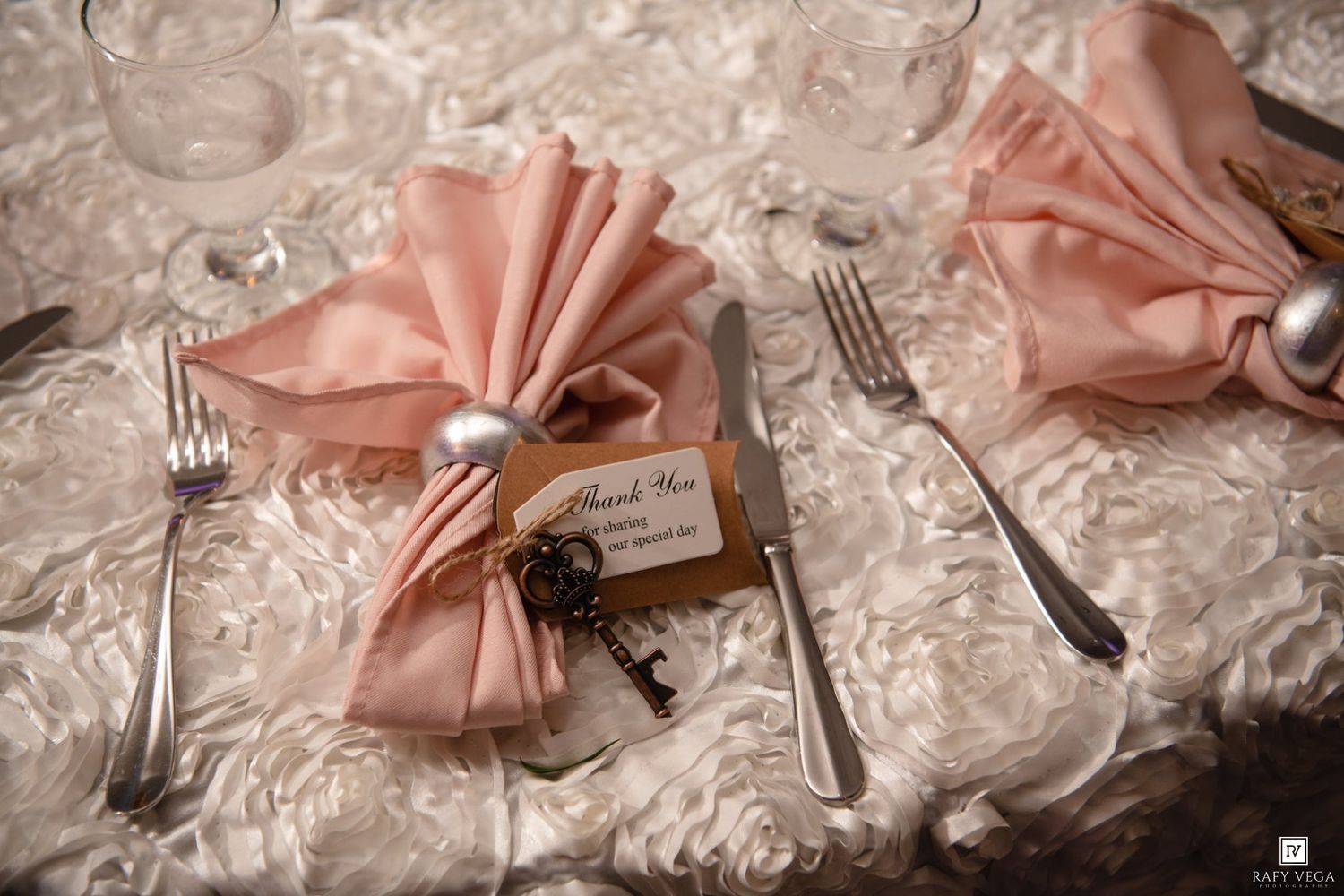 Elegant wedding table setting with blush pink folded napkins, silverware, and a thank you tag with vintage key favor.