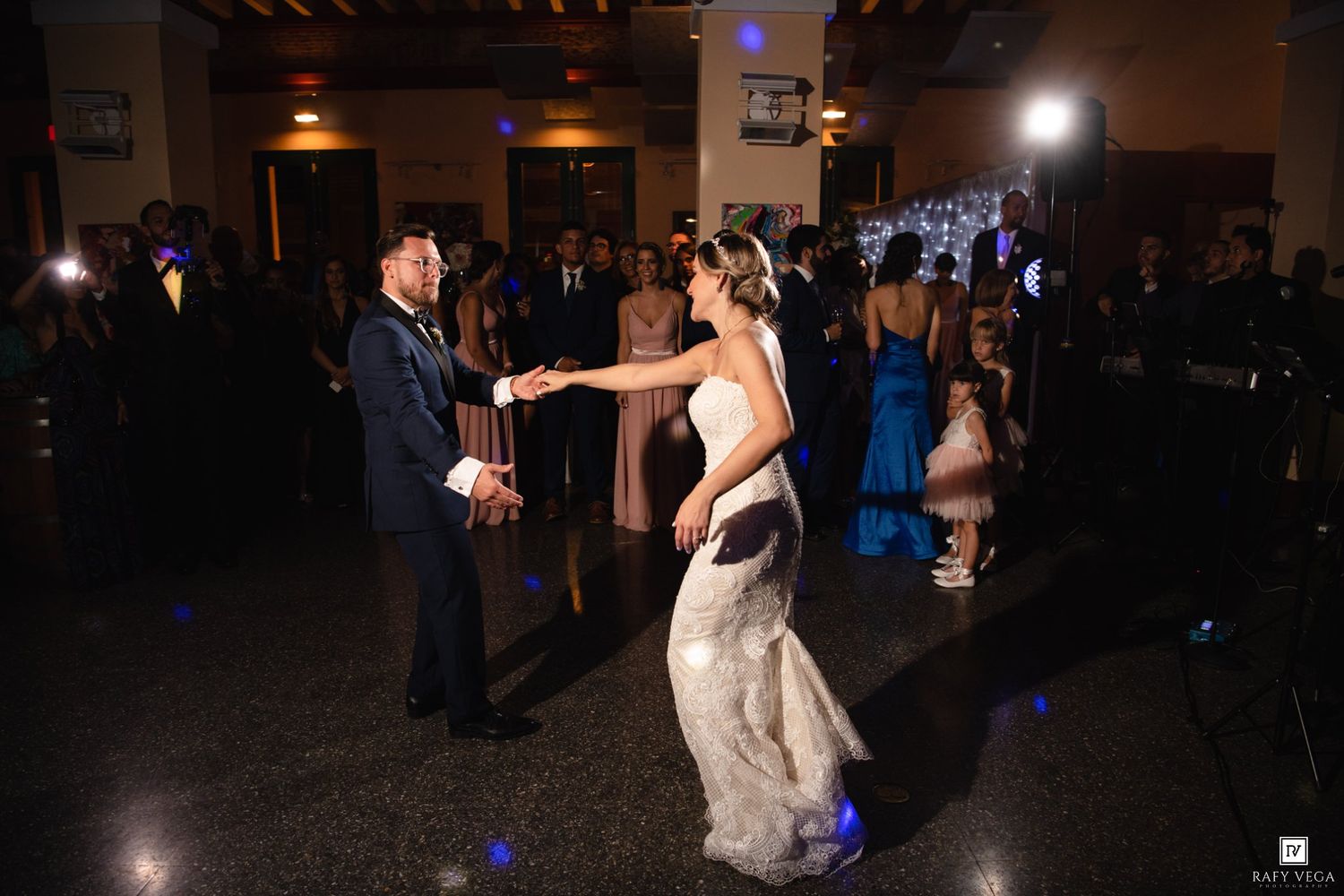 Bride and groom share their first dance surrounded by guests at wedding reception.