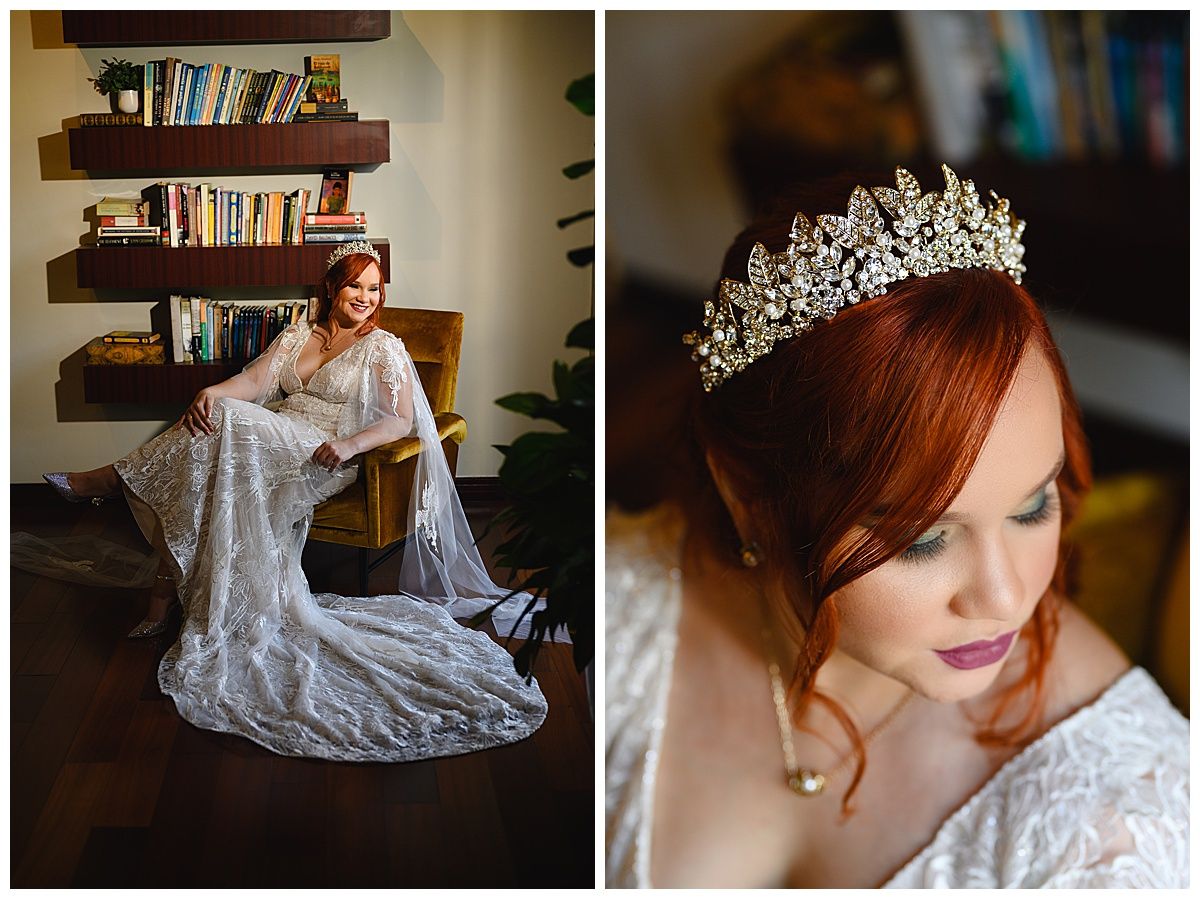 Red-haired bride in lace gown wearing ornate crystal crown poses elegantly in chair beside bookshelf.