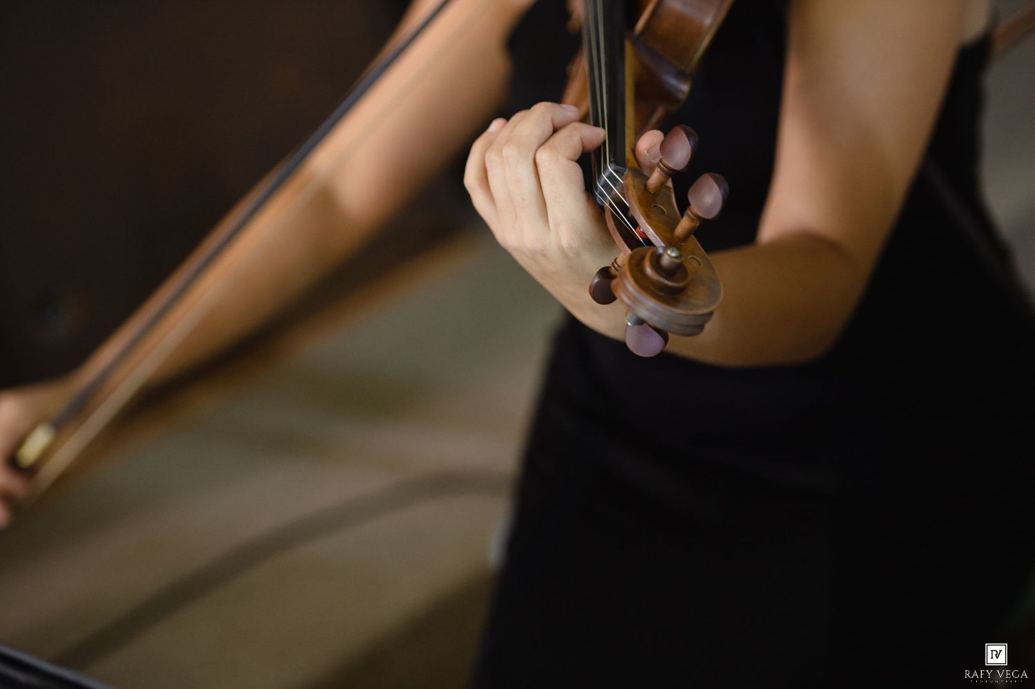 Close-up of a woman in black dress playing violin, fingers on strings, elegant musical performance.