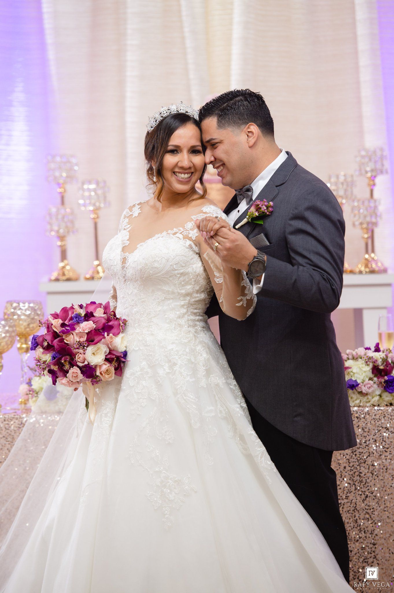 Bride in lace gown and groom in gray suit share a joyful moment at elegant wedding reception.