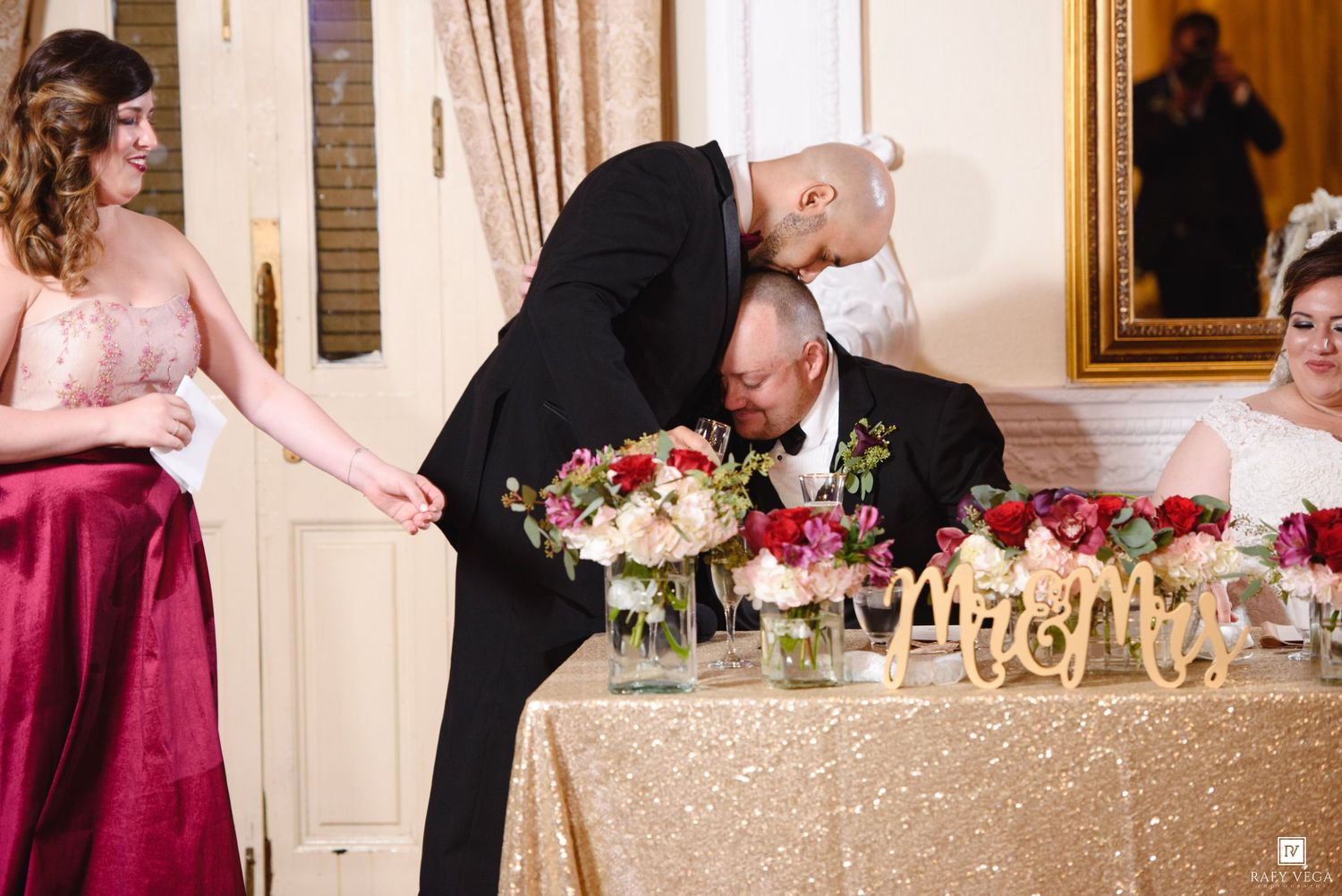 Groom kisses bride at elegant wedding reception table with gold Mr. and Mrs. signs and floral centerpieces.