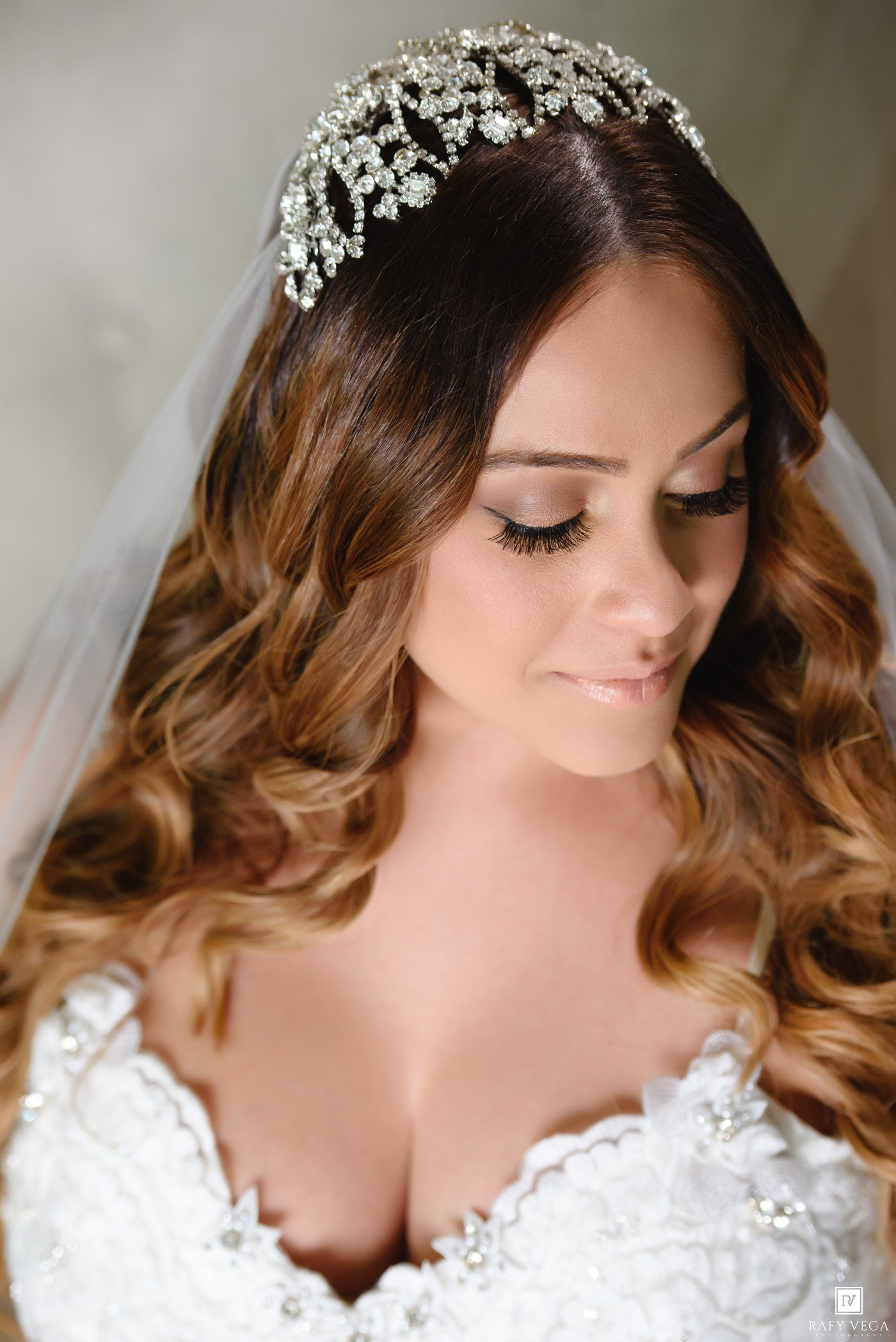 Bride wearing a sparkling crystal tiara and white lace wedding gown with soft curled hair and elegant bridal makeup.