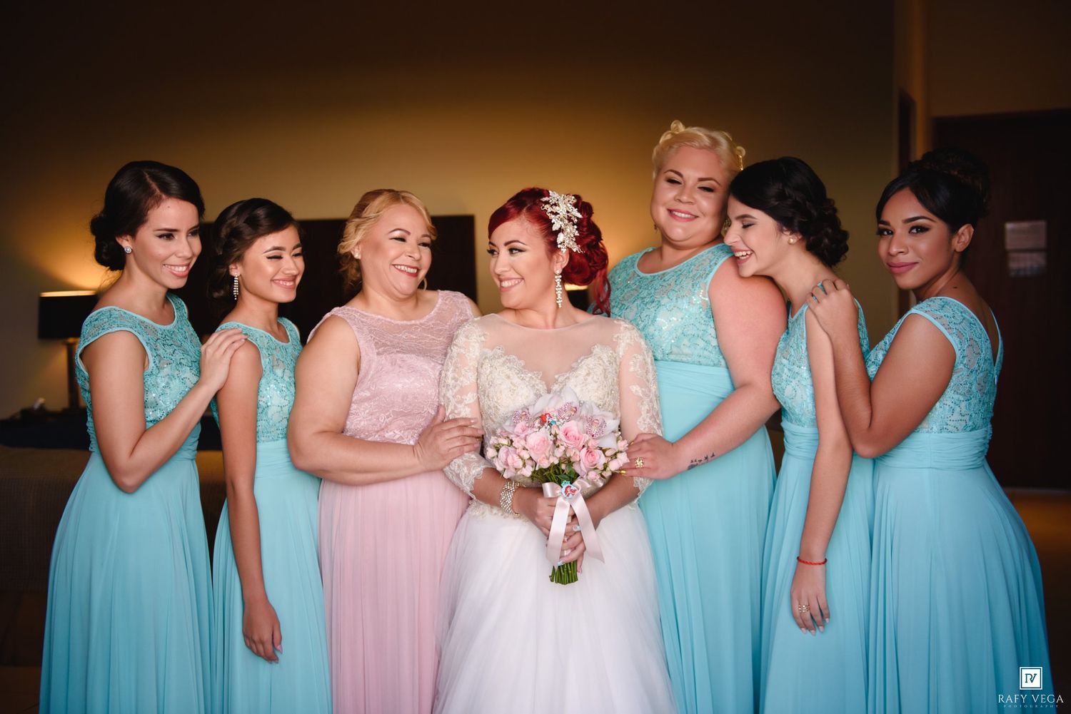 Bride in white gown holds pink bouquet surrounded by bridesmaids in blue and pink dresses at wedding.
