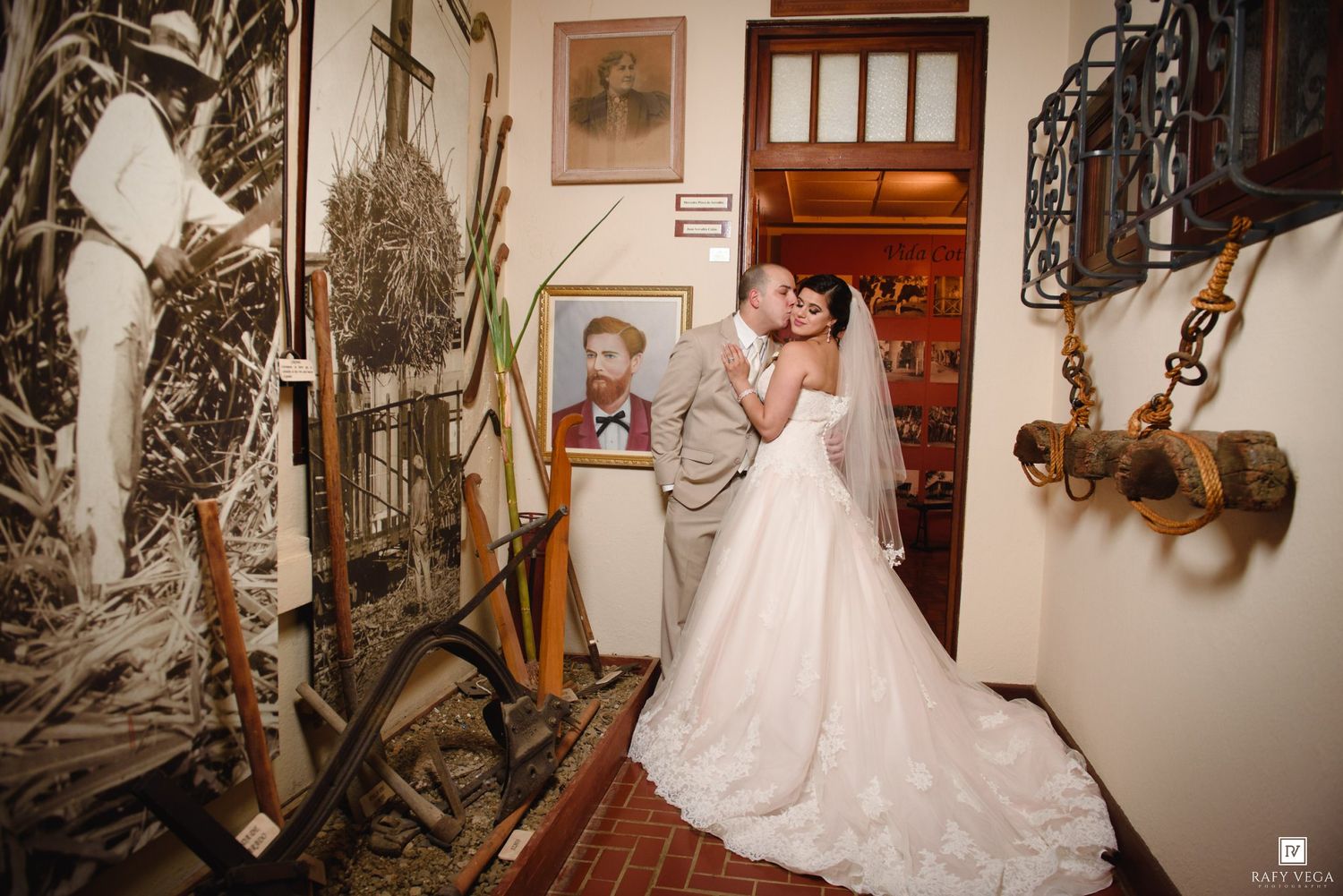 Bride and groom share a romantic kiss in a rustic museum hallway filled with antique artifacts and vintage decor.