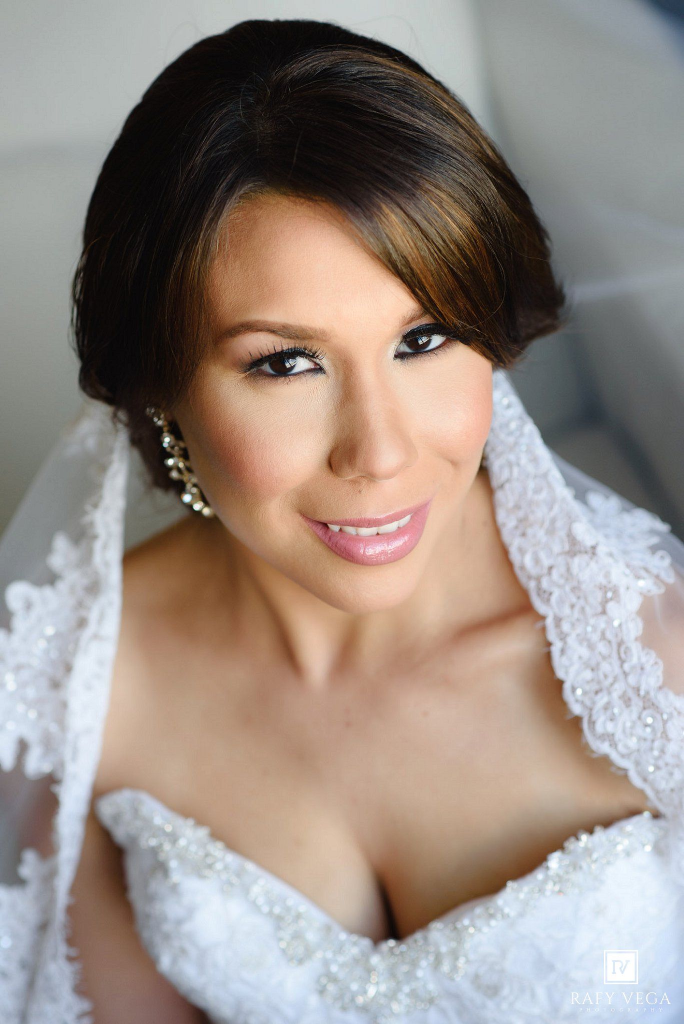 Elegant bride in lace wedding dress with pearl earrings and veil, wearing bridal makeup with smoky eyes and pink lips.