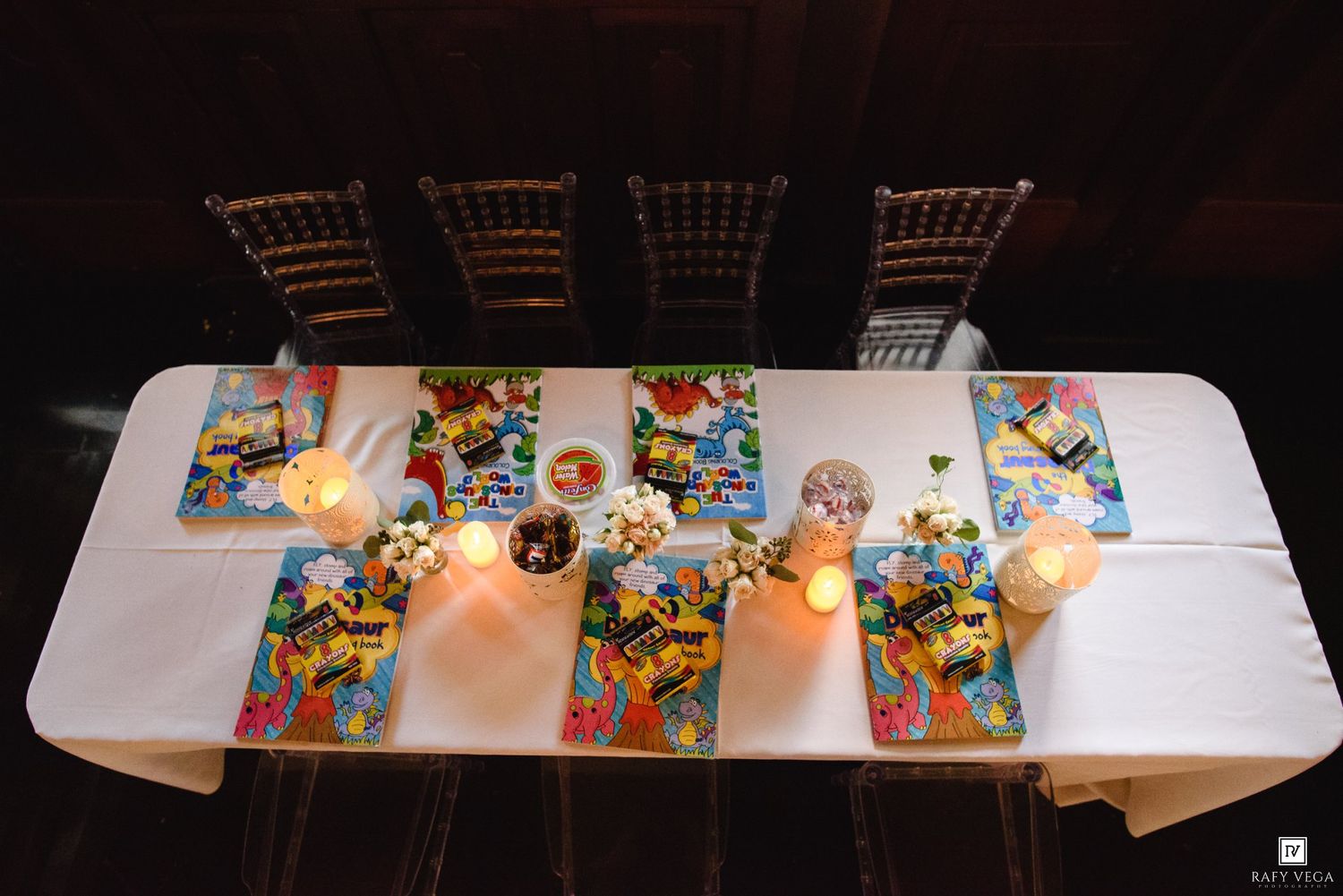 Overhead view of a white wedding reception table set with colorful comic book placemats, candles, and chiavari chairs.