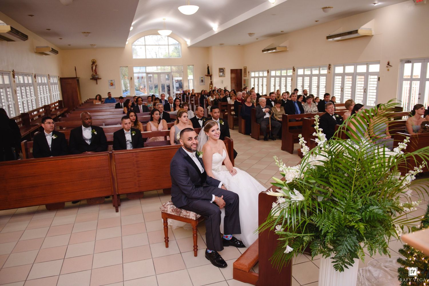 Bride and groom sit at altar during church wedding ceremony with guests in pews.