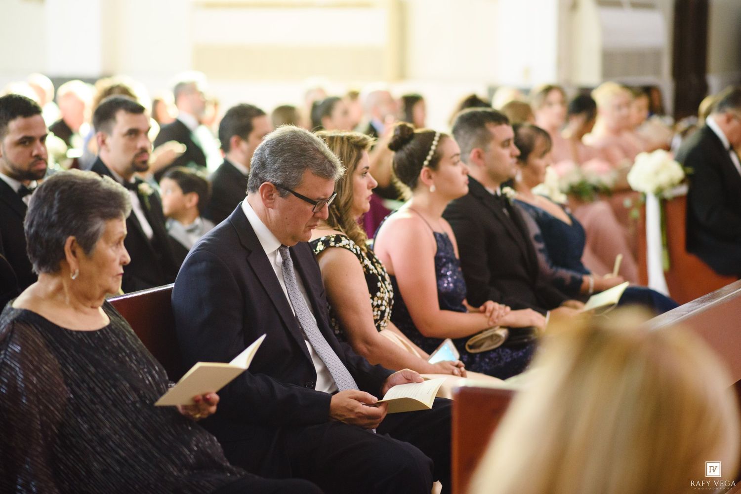 Wedding guests seated in church pews, reading programs during a formal ceremony.