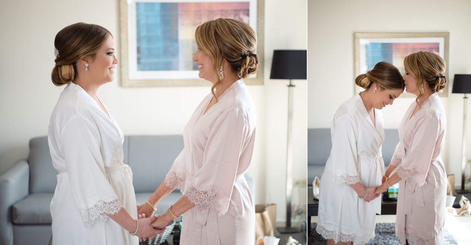 Two brides in white robes hold hands and share a tender moment while getting ready for their wedding day.