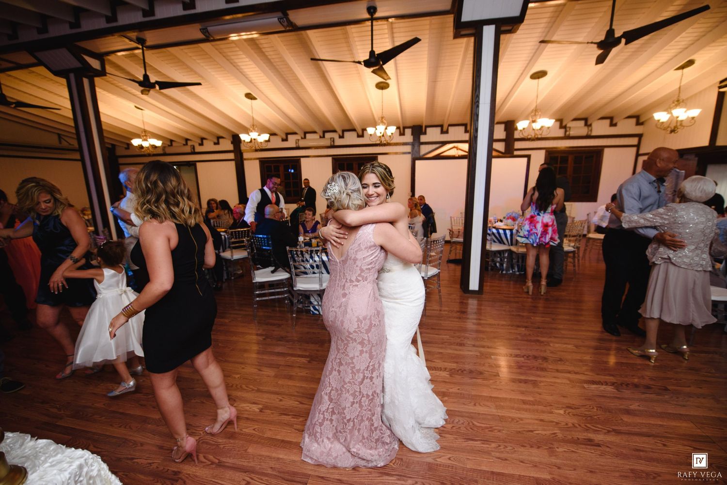 Bride and bridesmaid share a warm hug on the dance floor at a wedding reception.