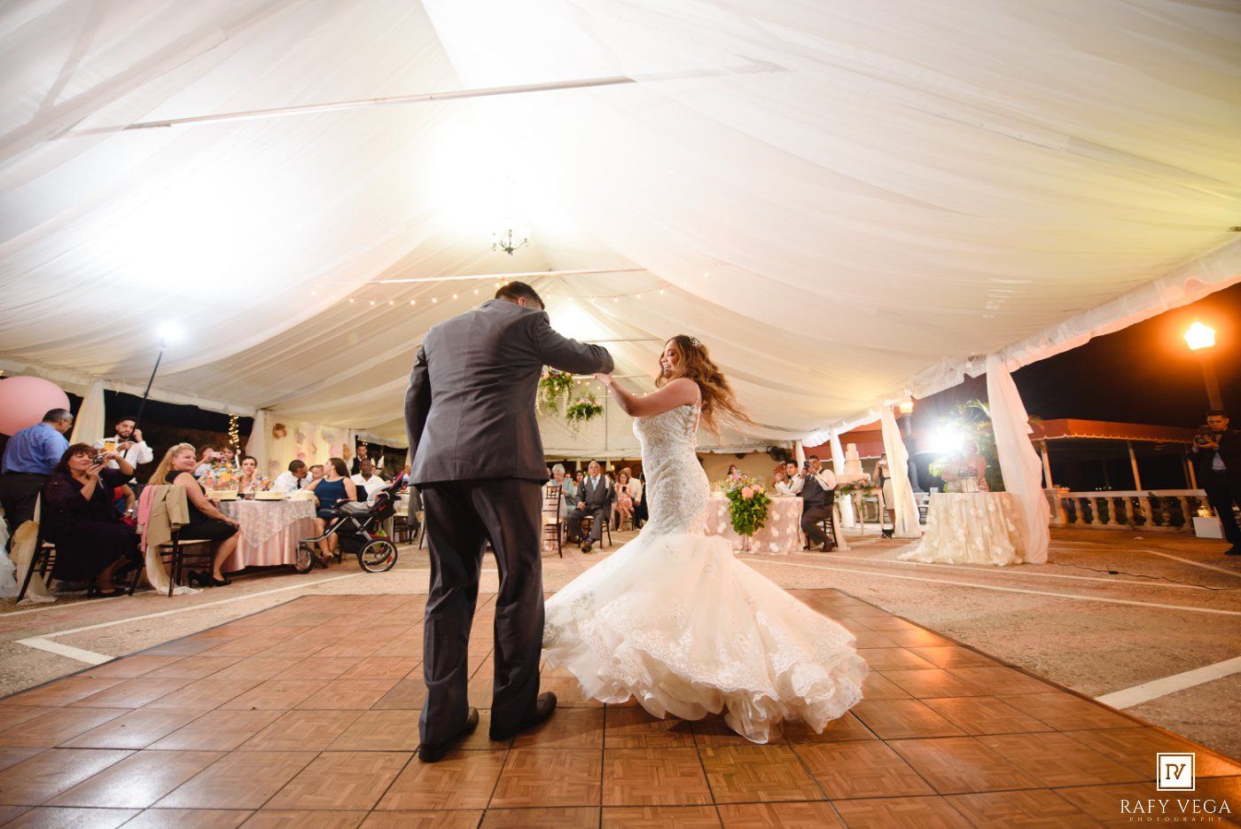 Bride and groom share first dance under white tent at elegant outdoor wedding reception.