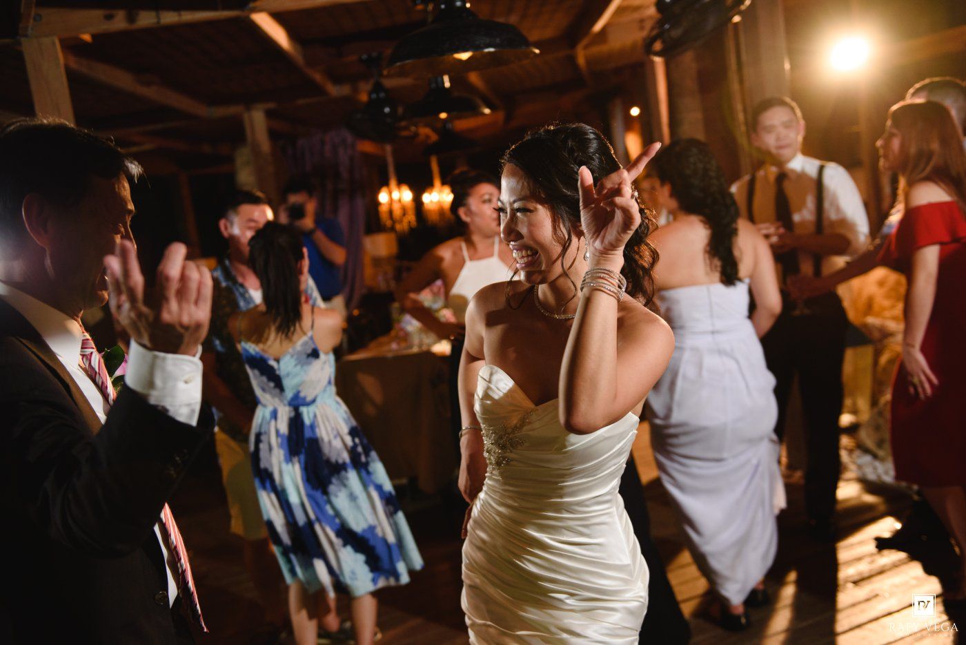 Bride in white strapless gown dancing with guests at a warmly lit wedding reception party.