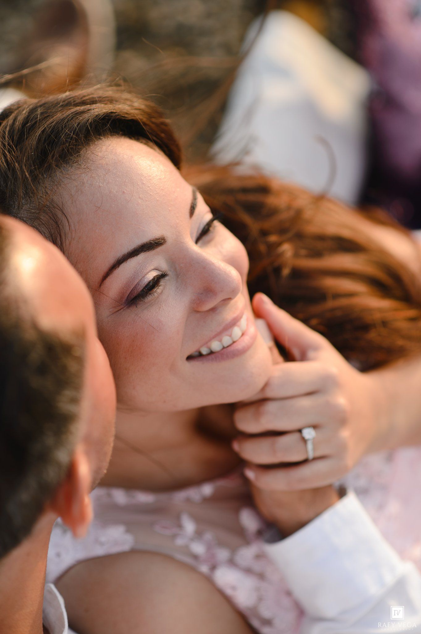 A smiling bride with freckles and an engagement ring gazes lovingly at her groom during a romantic outdoor photo session.