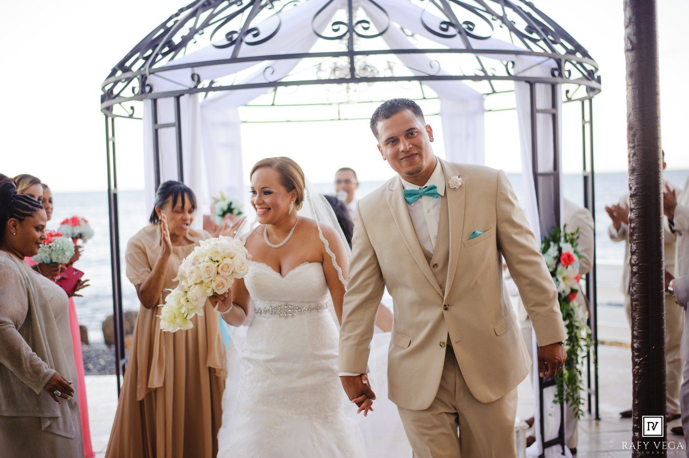Bride and groom walk hand-in-hand beneath an elegant gazebo after their outdoor wedding ceremony.