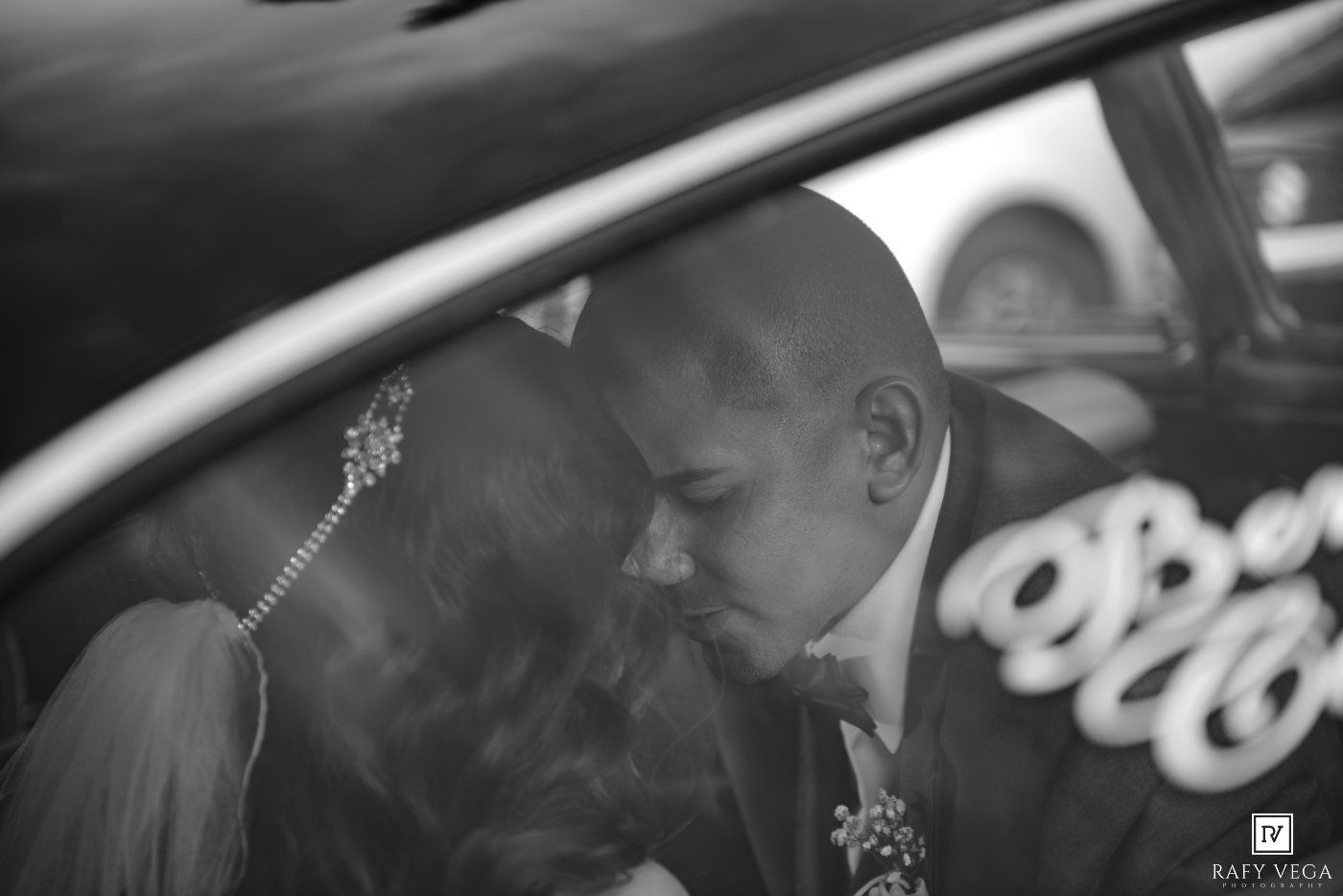 Black and white photo of a couple sharing a kiss inside a car on their wedding day.